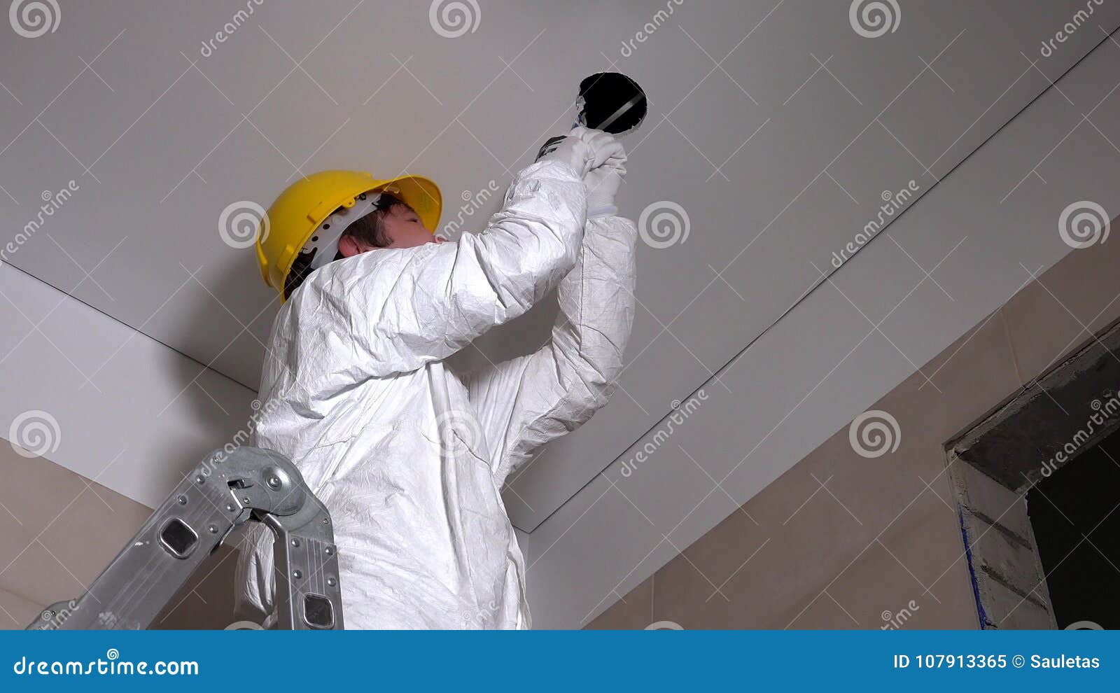 Male Worker With Helmet Cut Holes In Plasterboard Ceiling For Light Installation