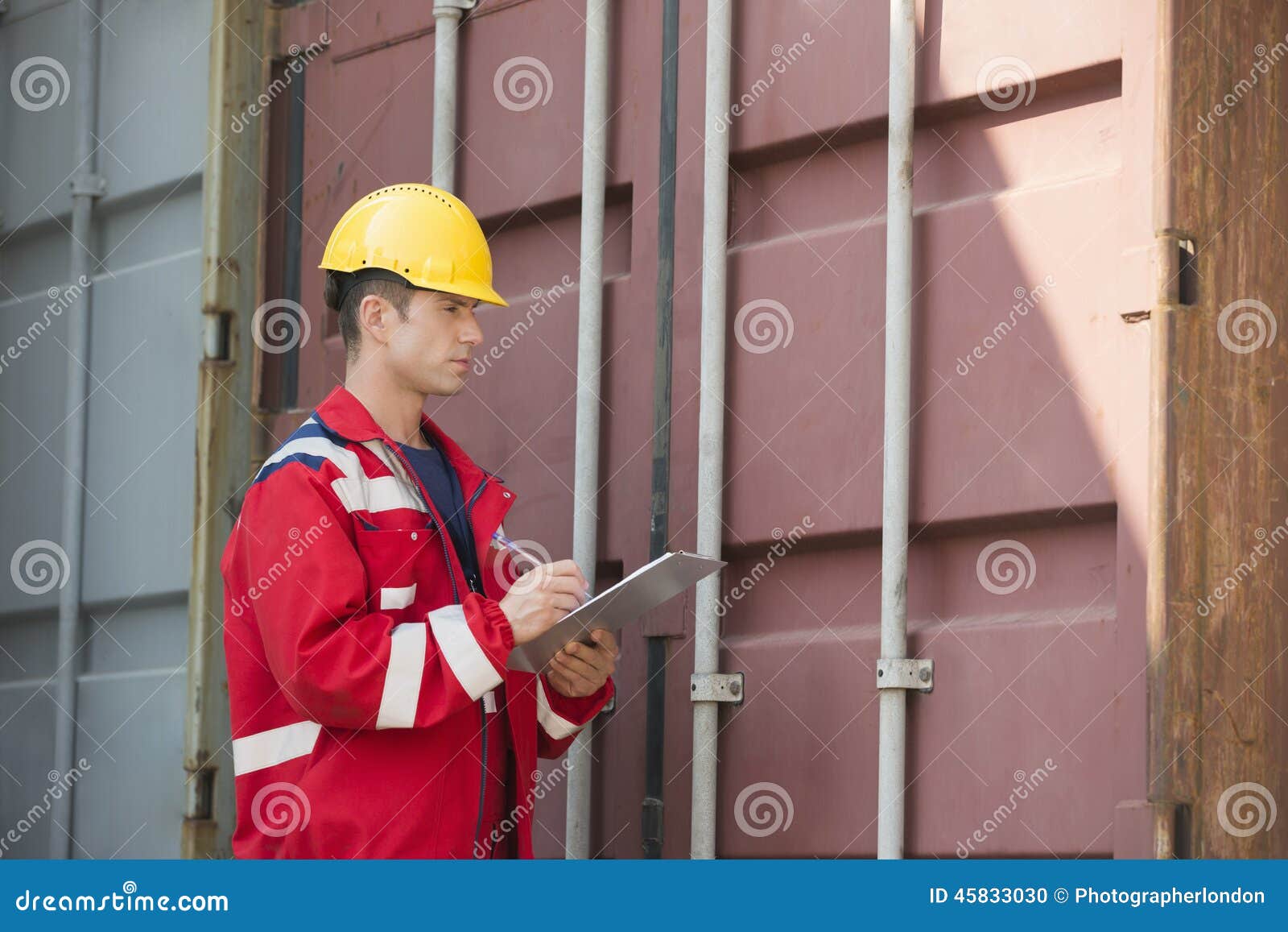 Male Worker Inspecting Cargo Container while Writing on Clipboard in
