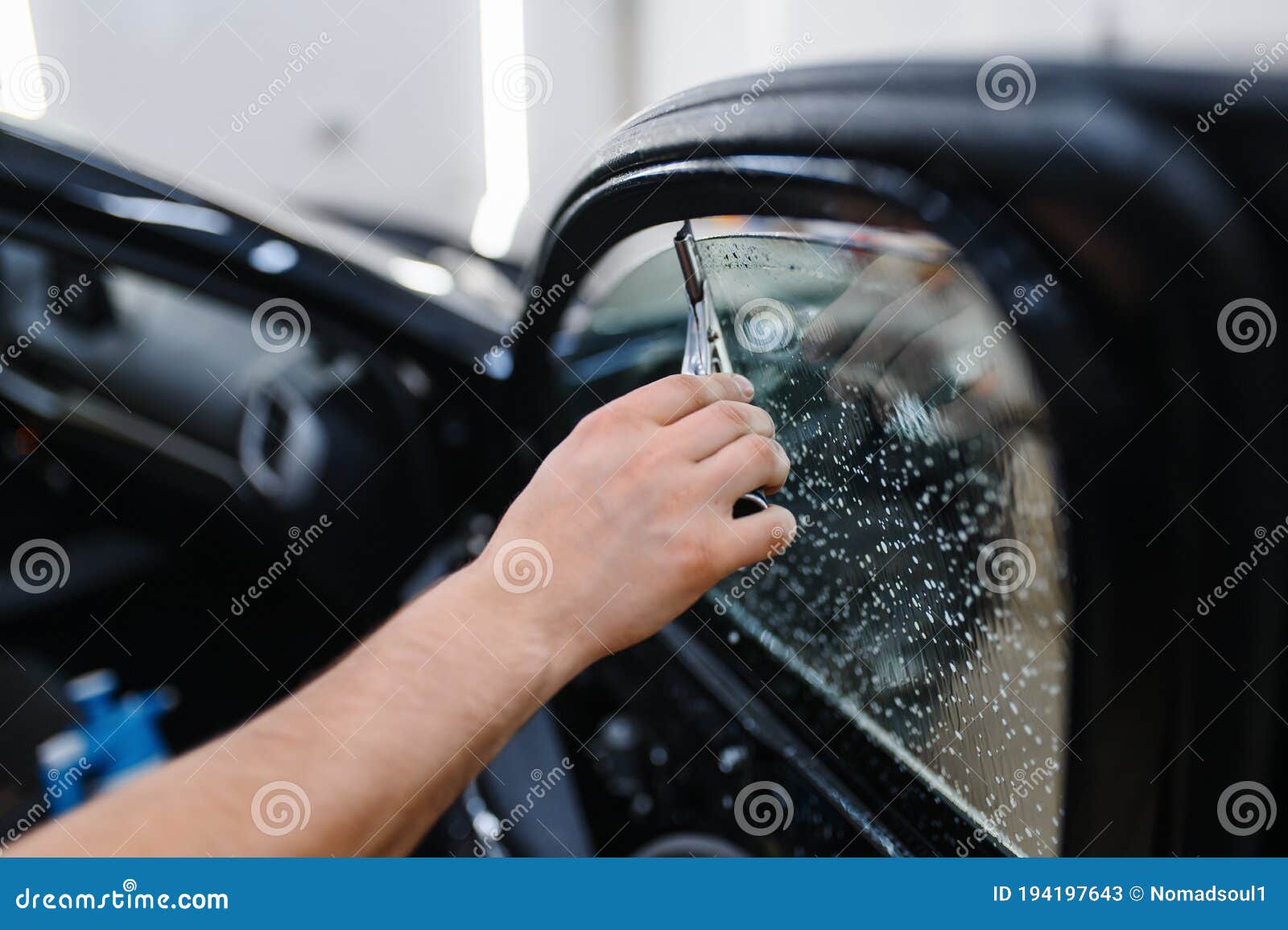 male worker with squeegee wipes car tinting