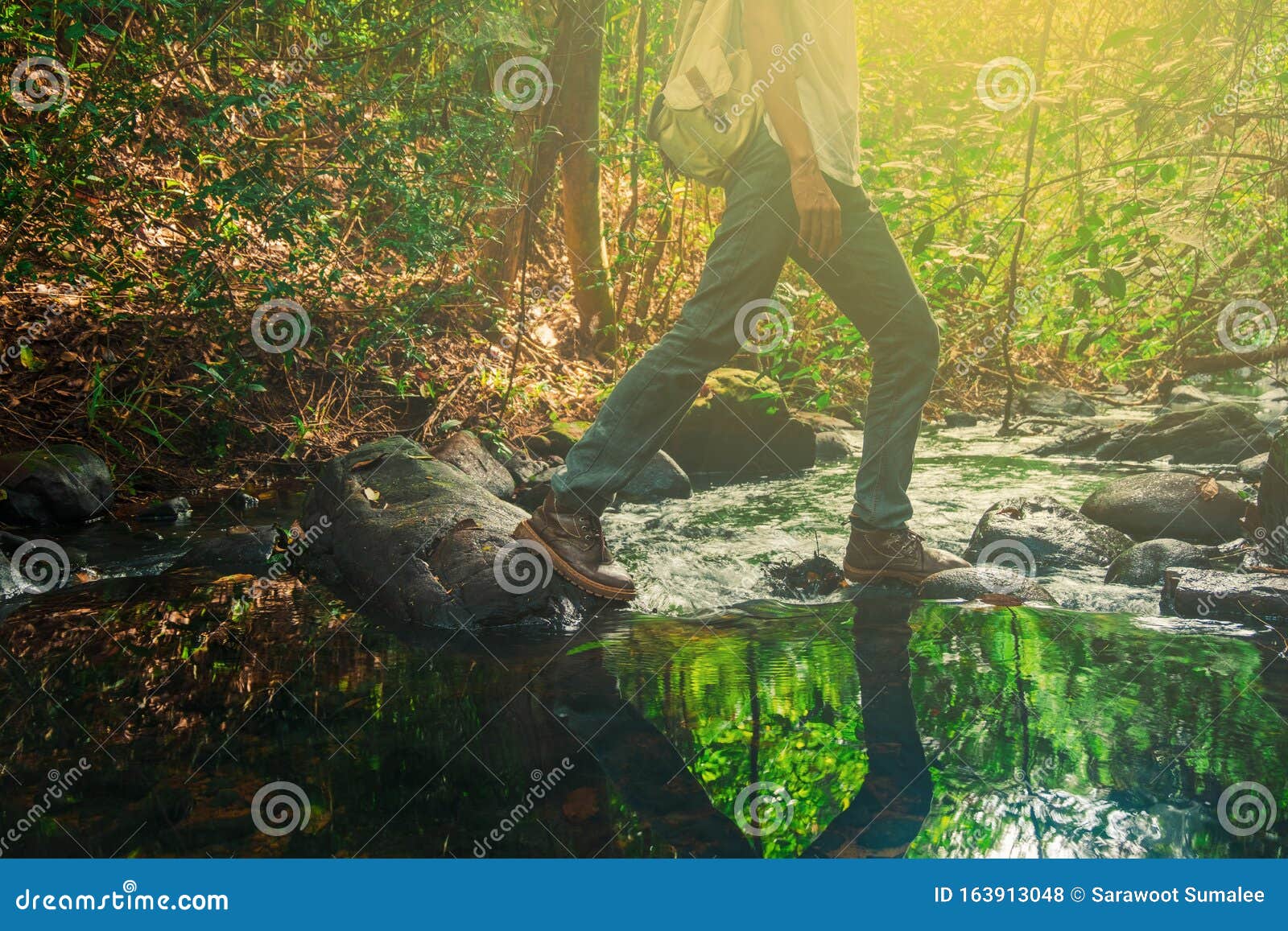 a man adventurer with backpack walking to cross  the stream in the forest.concept of forest travel vacations in forest,thailand,p