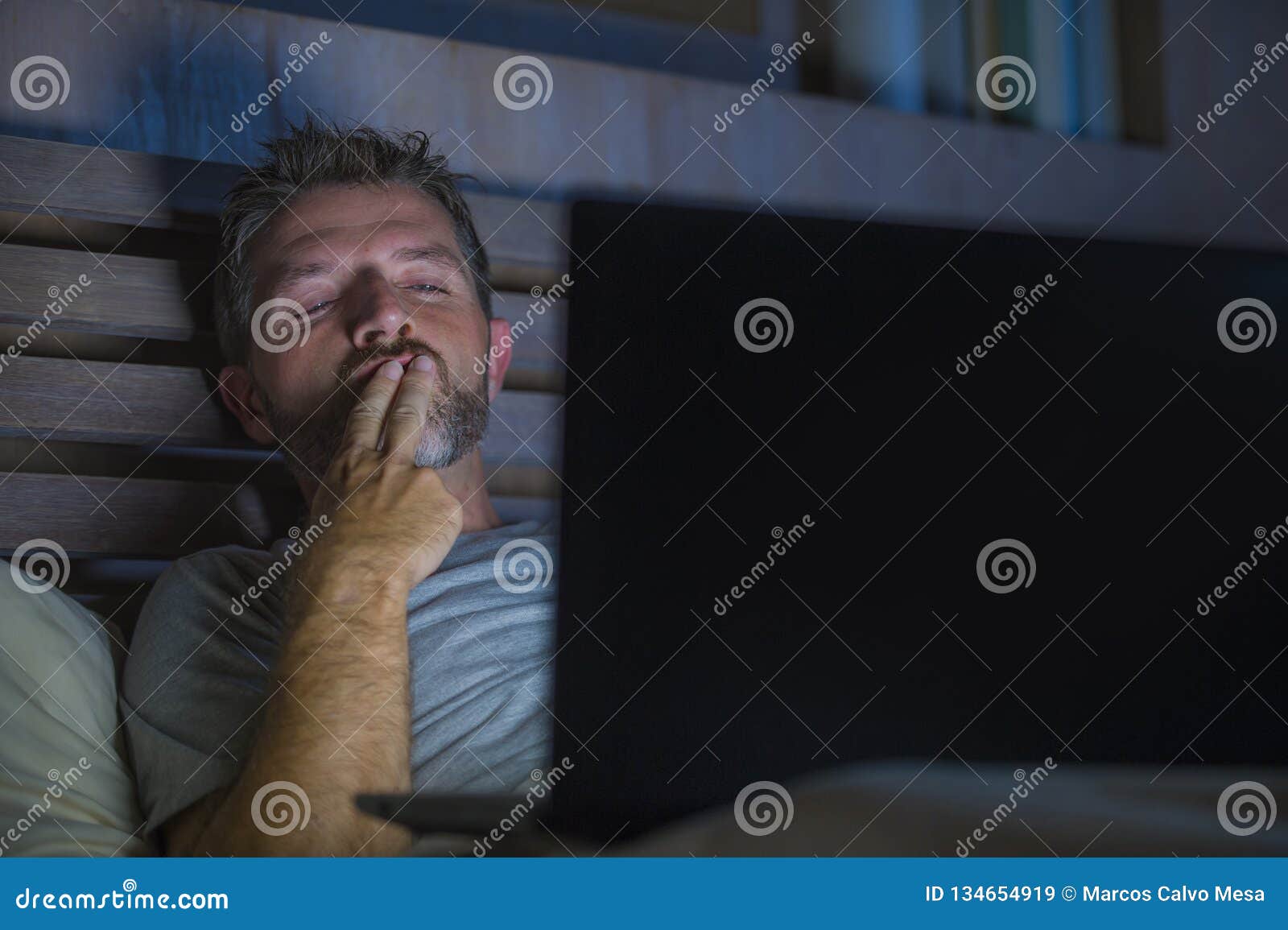 Man Alone in Bed Playing Cybersex Using Laptop Computer Watching Sex Movie Late at Night with Lascivious Pervert Face Stock Image photo