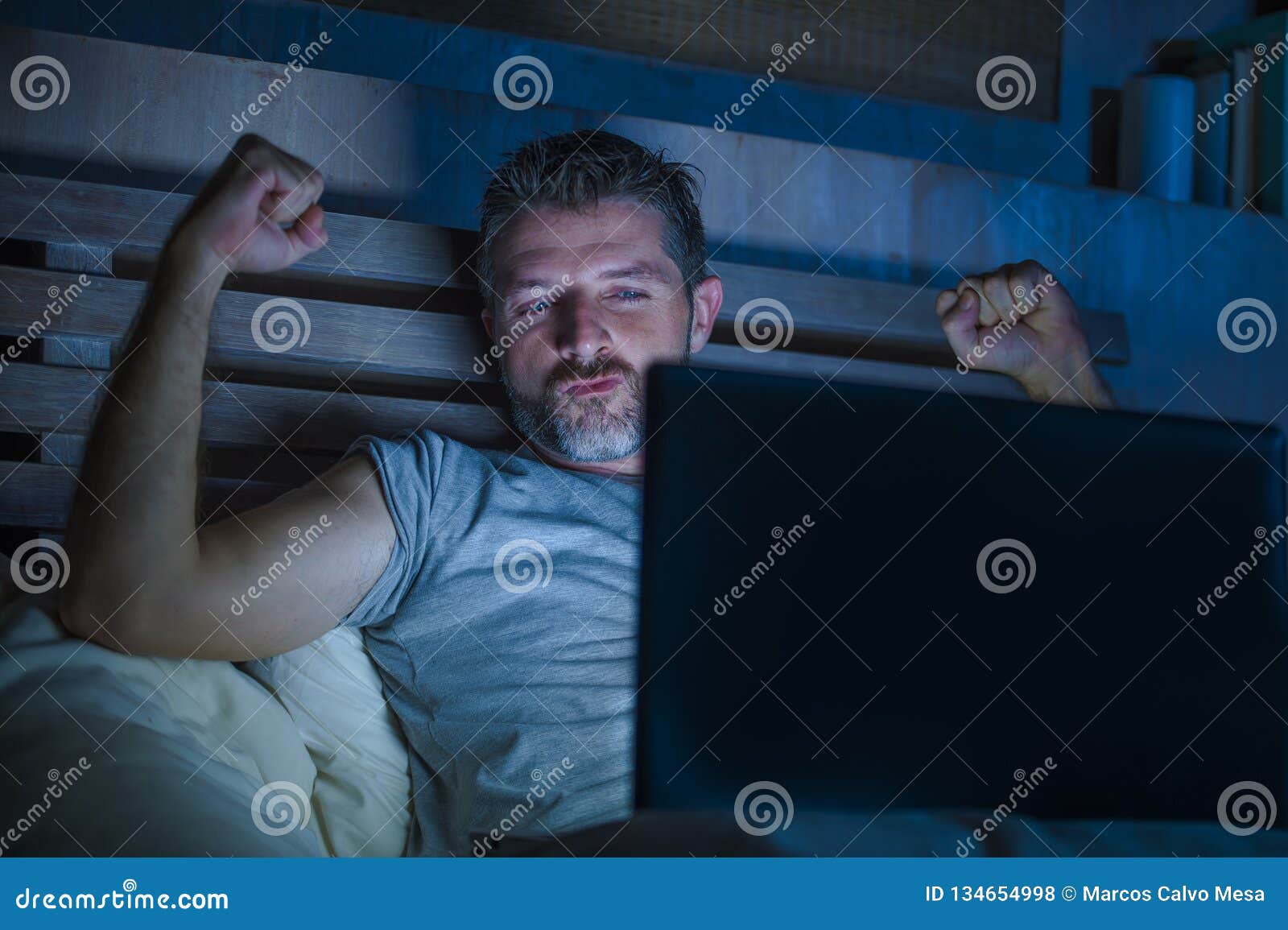 Man Alone in Bed Playing Cybersex Using Laptop Computer Watching Sex Movie Late at Night with Lascivious Pervert Face Stock Photo