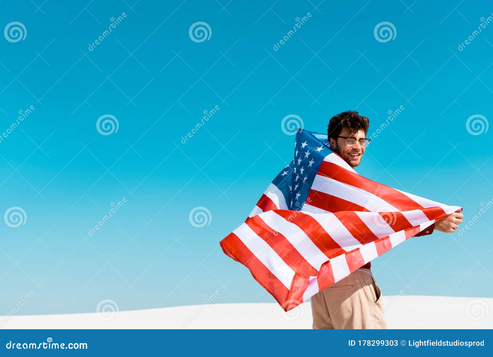 Man With American Flag On Windy Sandy Beach Against Clear Blue Sky