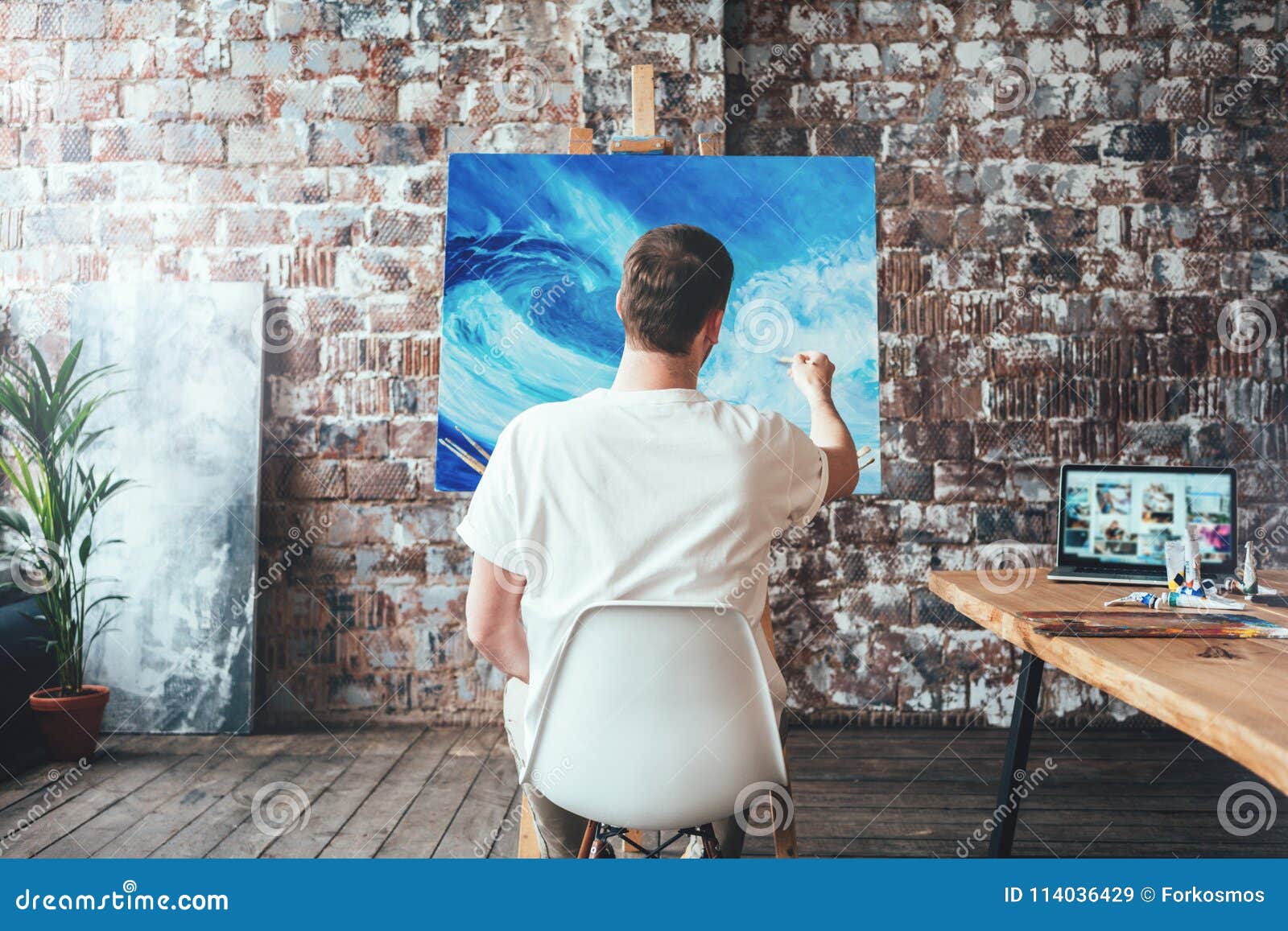 Man Artist Sitting on Chair in Front of Canvas on Easel and Drawing