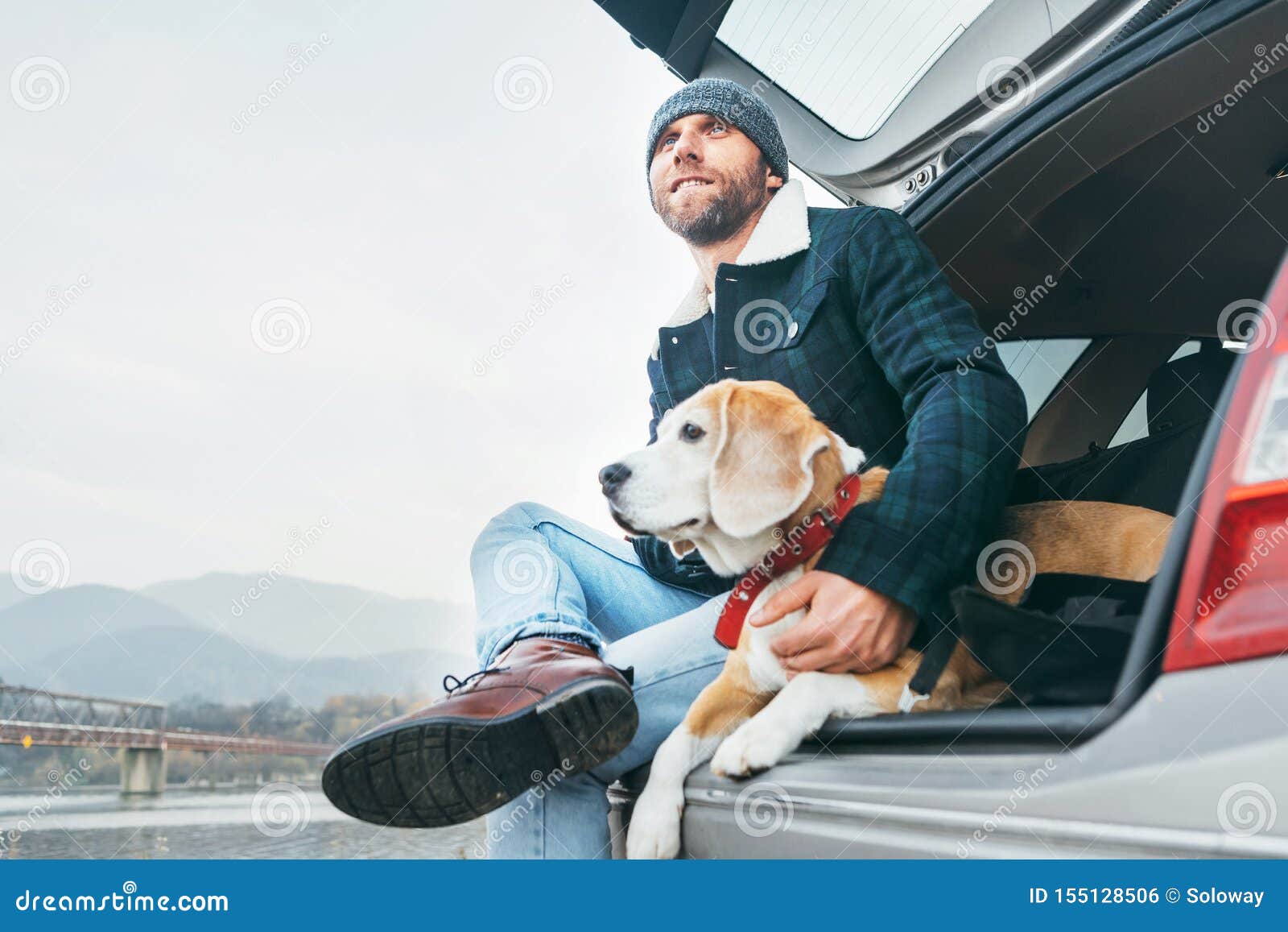 man with beagle dog siting together in car trunk