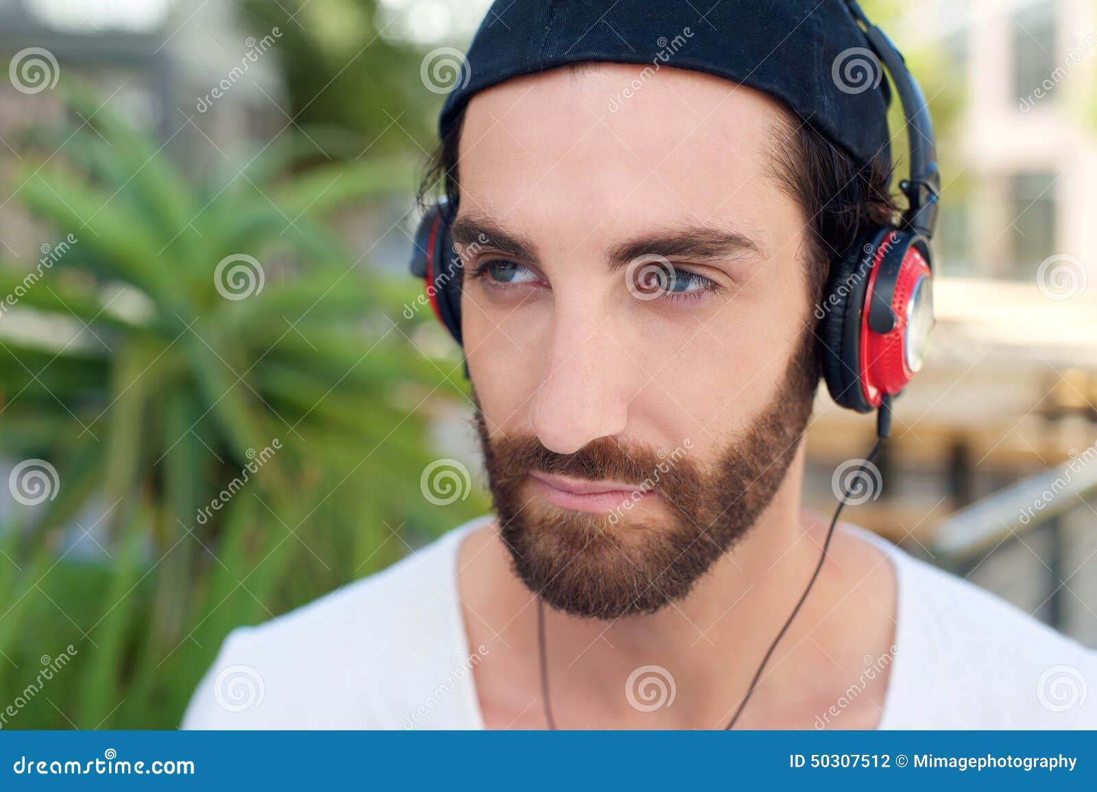 Close up portrait of a young man with beard listening to music on headphones