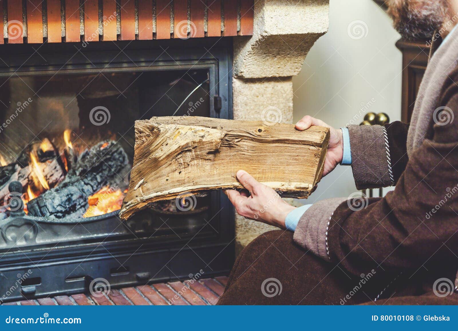 Man with Beard Wearing Bathrobe Puts Log in Burning Fireplace Stock