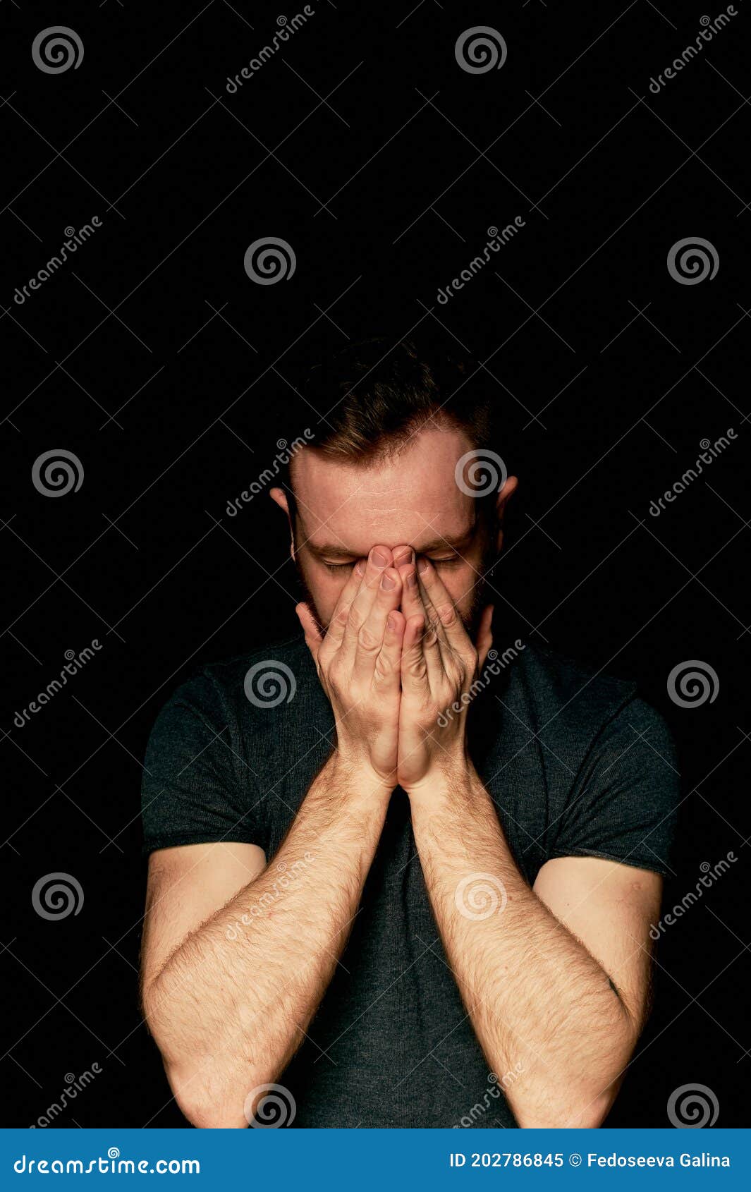 a man on a black background covers his face with his hands. the atmosphere of hopelessness,dejection