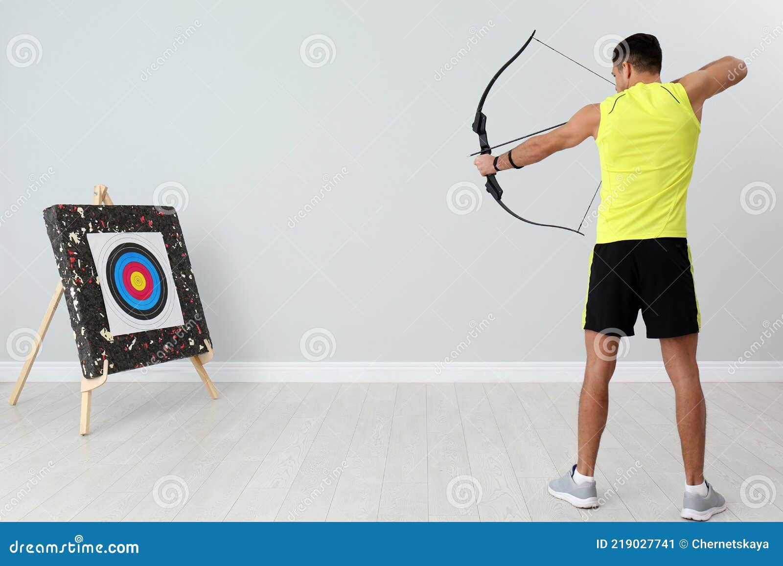 Man with Bow and Arrow Aiming at Archery Target Indoors Stock Image