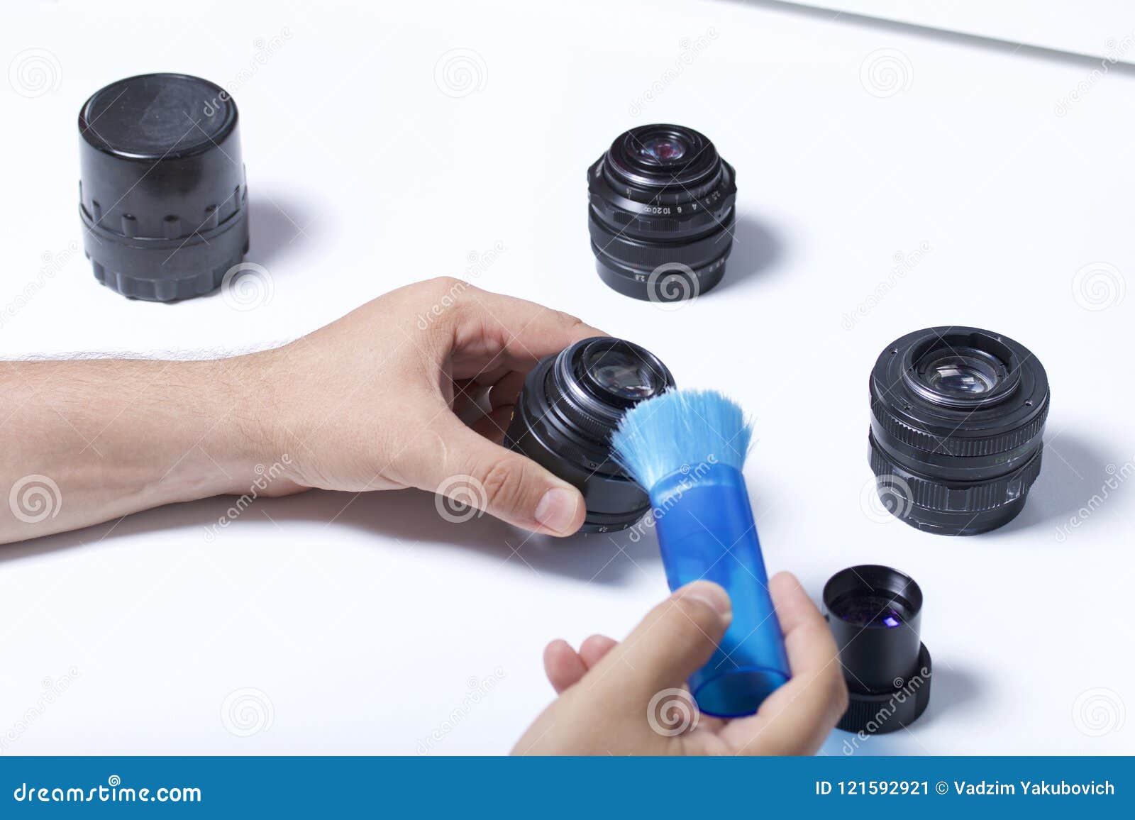 the man is brushing the dust off the lens of the lens with a brush. nearby on the table are other vintage lenses.
