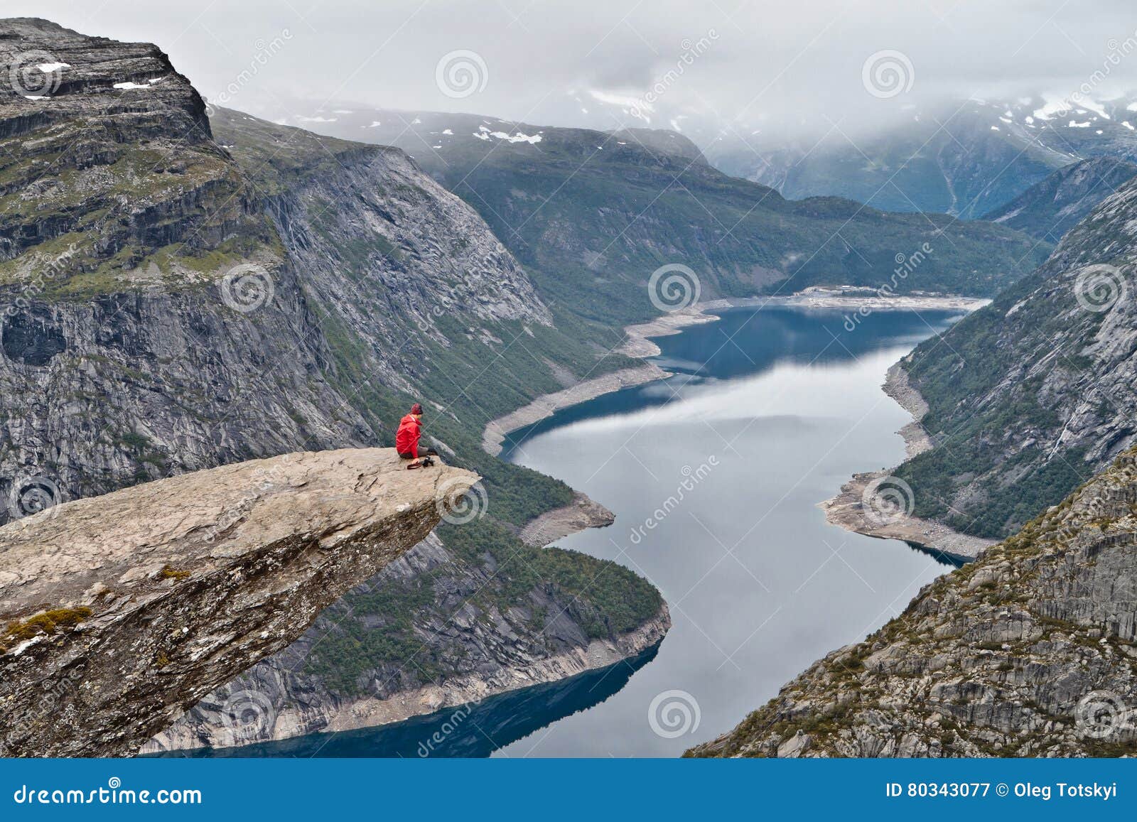 Man with camera sitting on Trolltunga rock Troll`s Tongue rock and looking at Norwegian mountain landscape