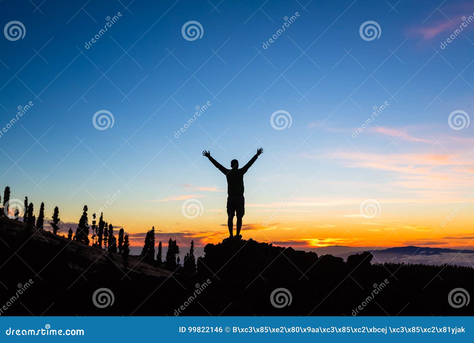 man celebrating sunset with arms outstretched in mountains