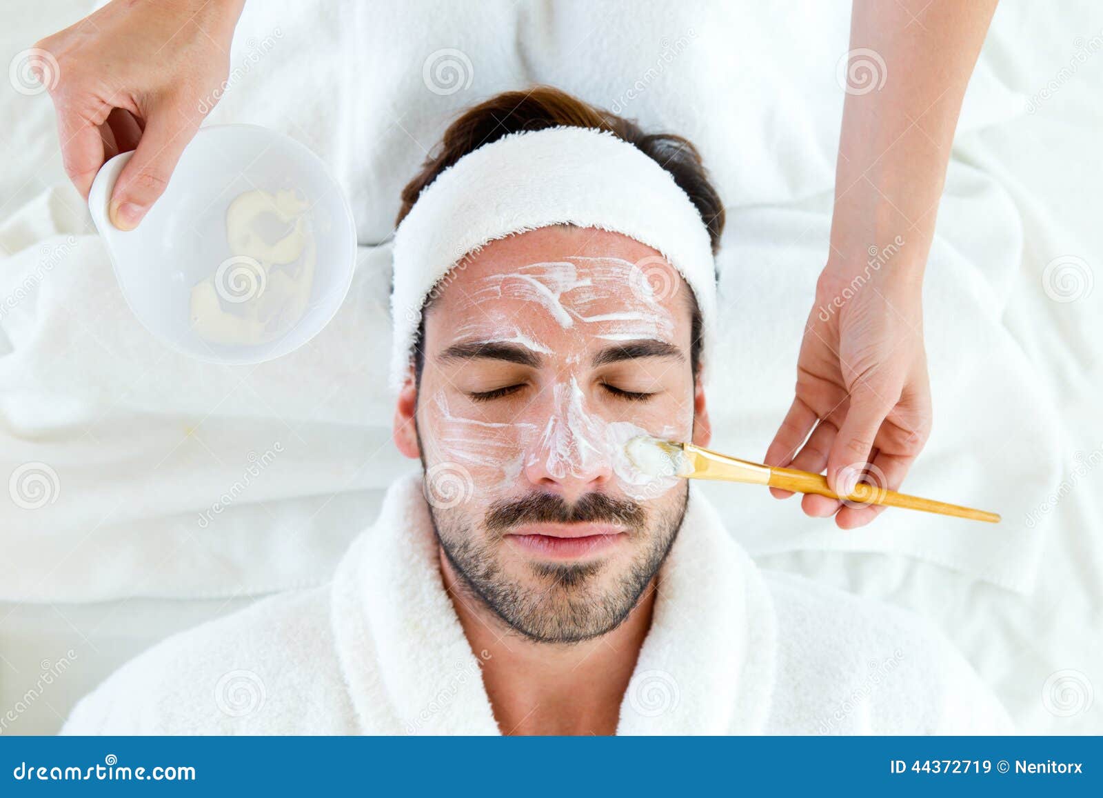 man with clay facial mask in beauty spa.