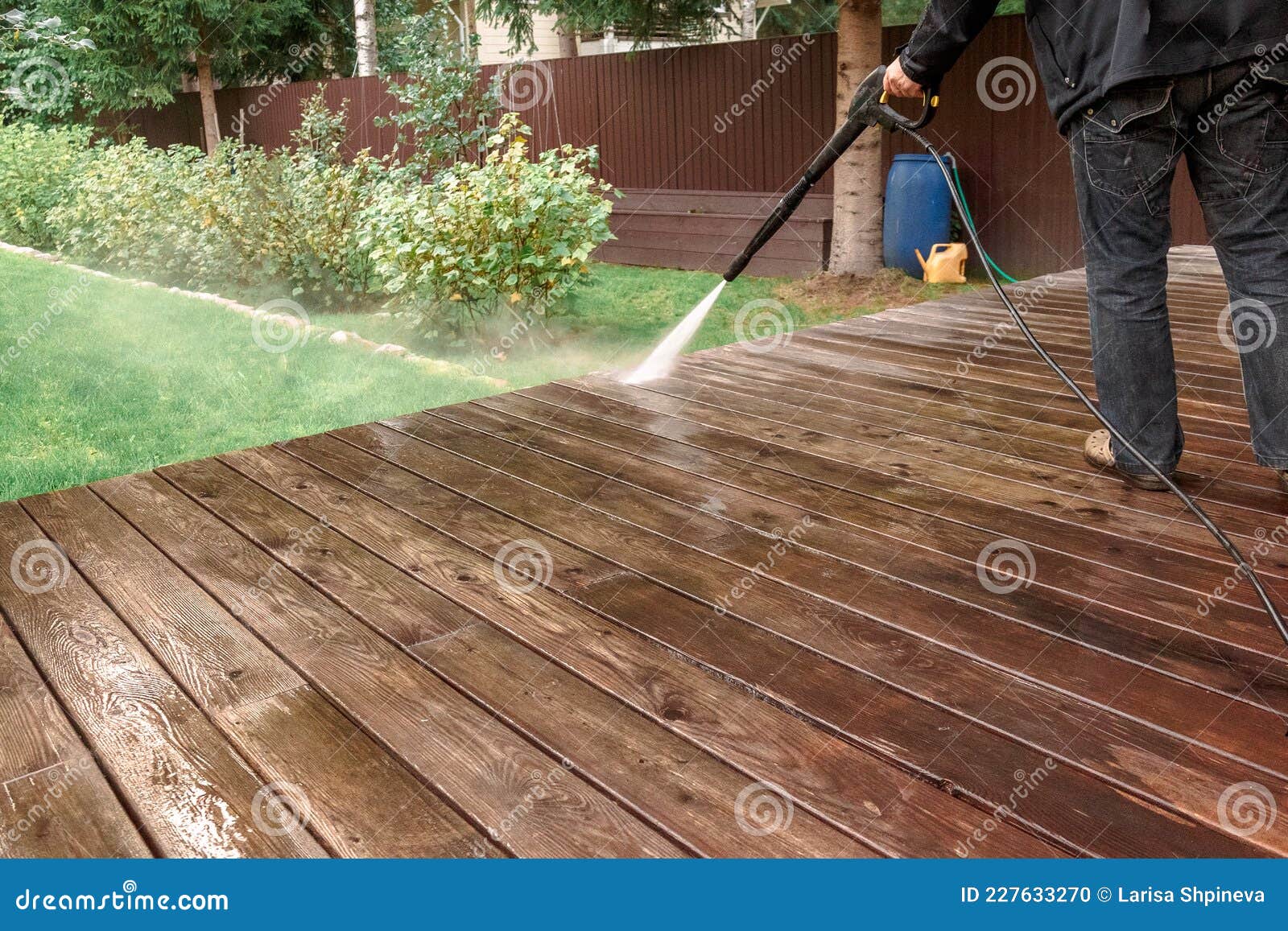 man cleaning walls and floor with high pressure power washer. washing terrace wood planks and cladding walls.
