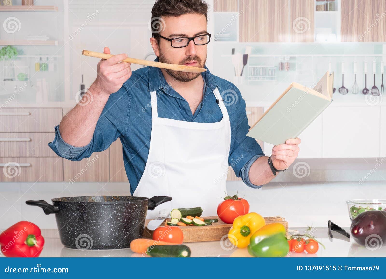 Man Cooking At Home Reading From Recipe Book Stock Image - Image of
