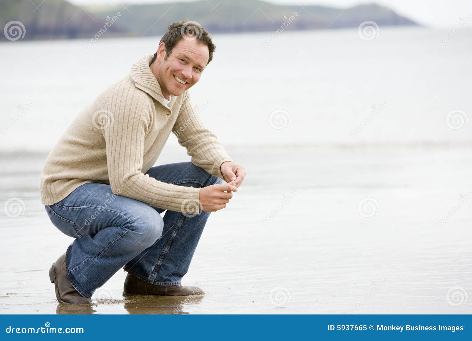 man crouching on beach
