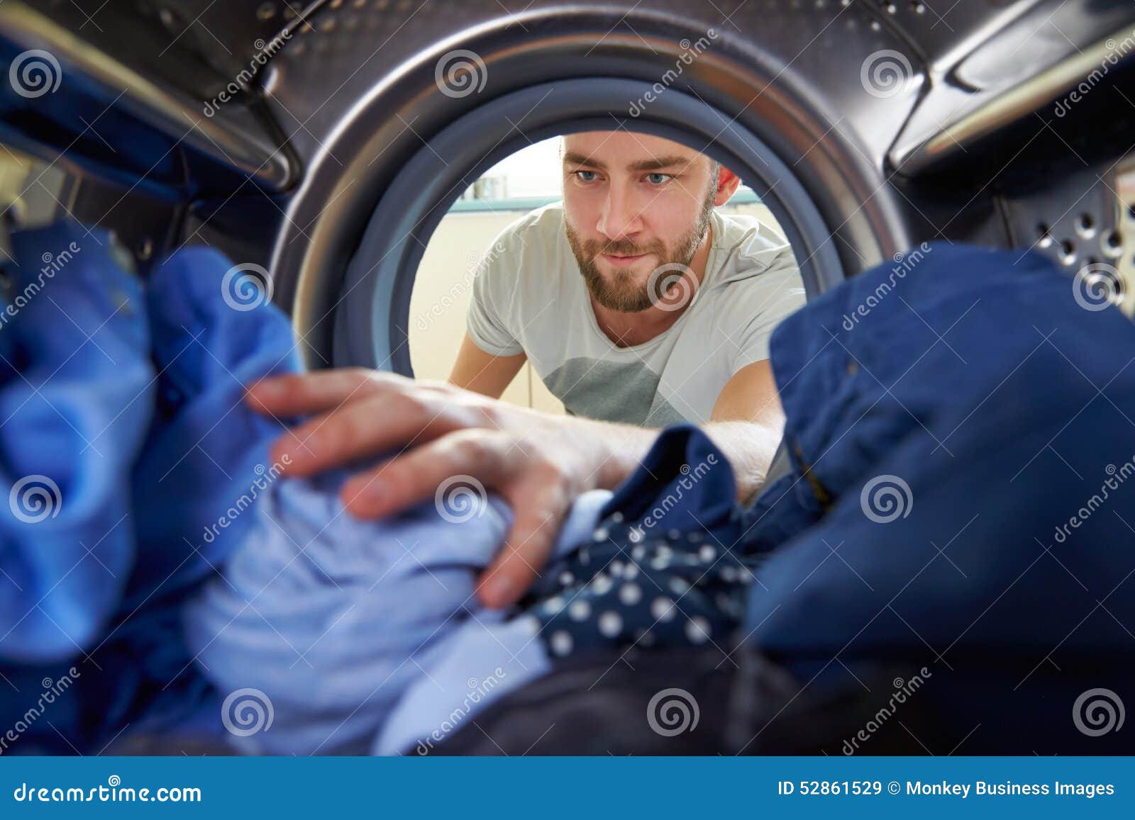 man doing laundry reaching inside washing machine