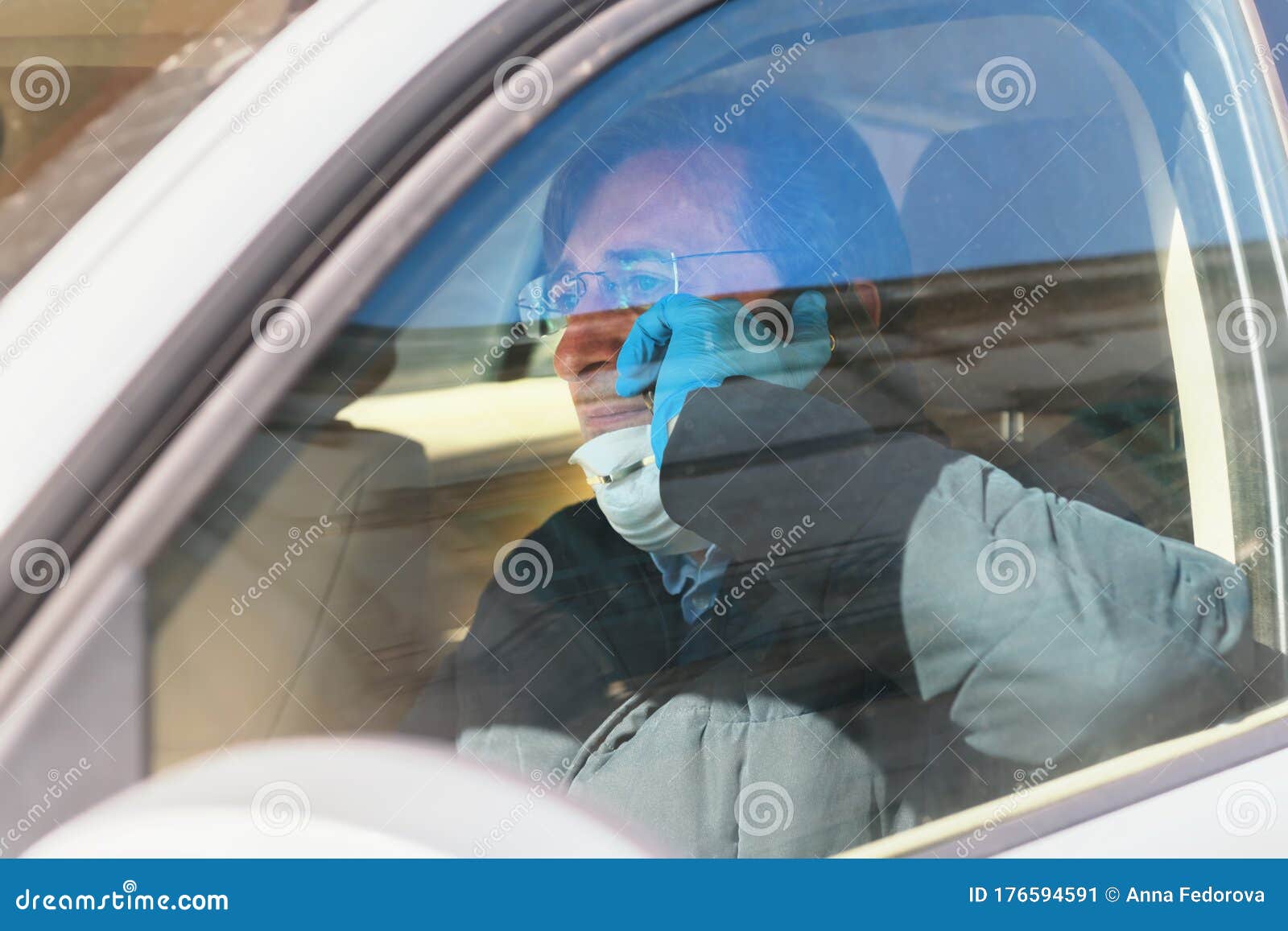 a man driving in a car with a protective mask and gloves is talking on the phone, epidemia of coronavirus. work during quarantine