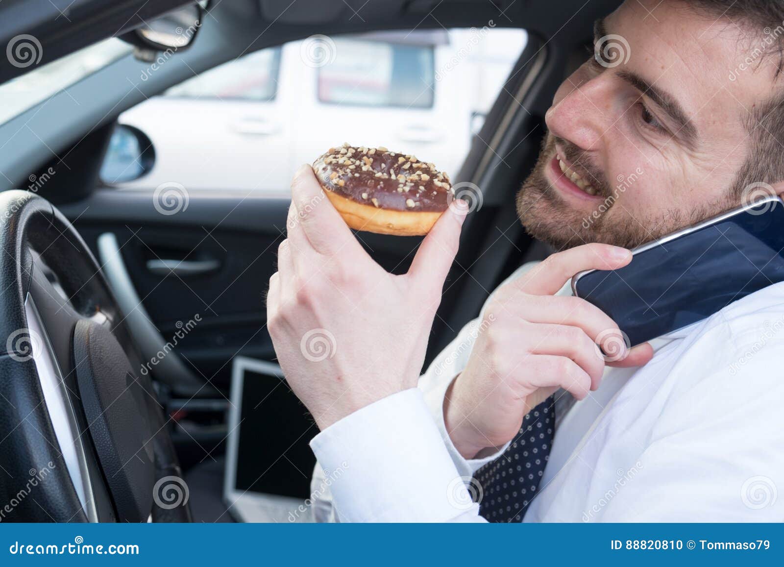 Man Eating a Doughnut and Talking on the Phone Driving Car Stock Photo