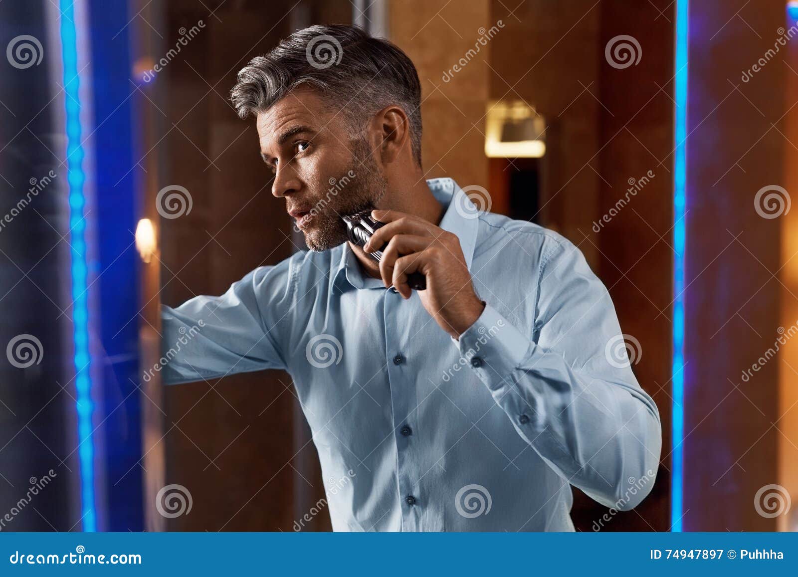 man with electric razor shaving face in bathroom. men grooming