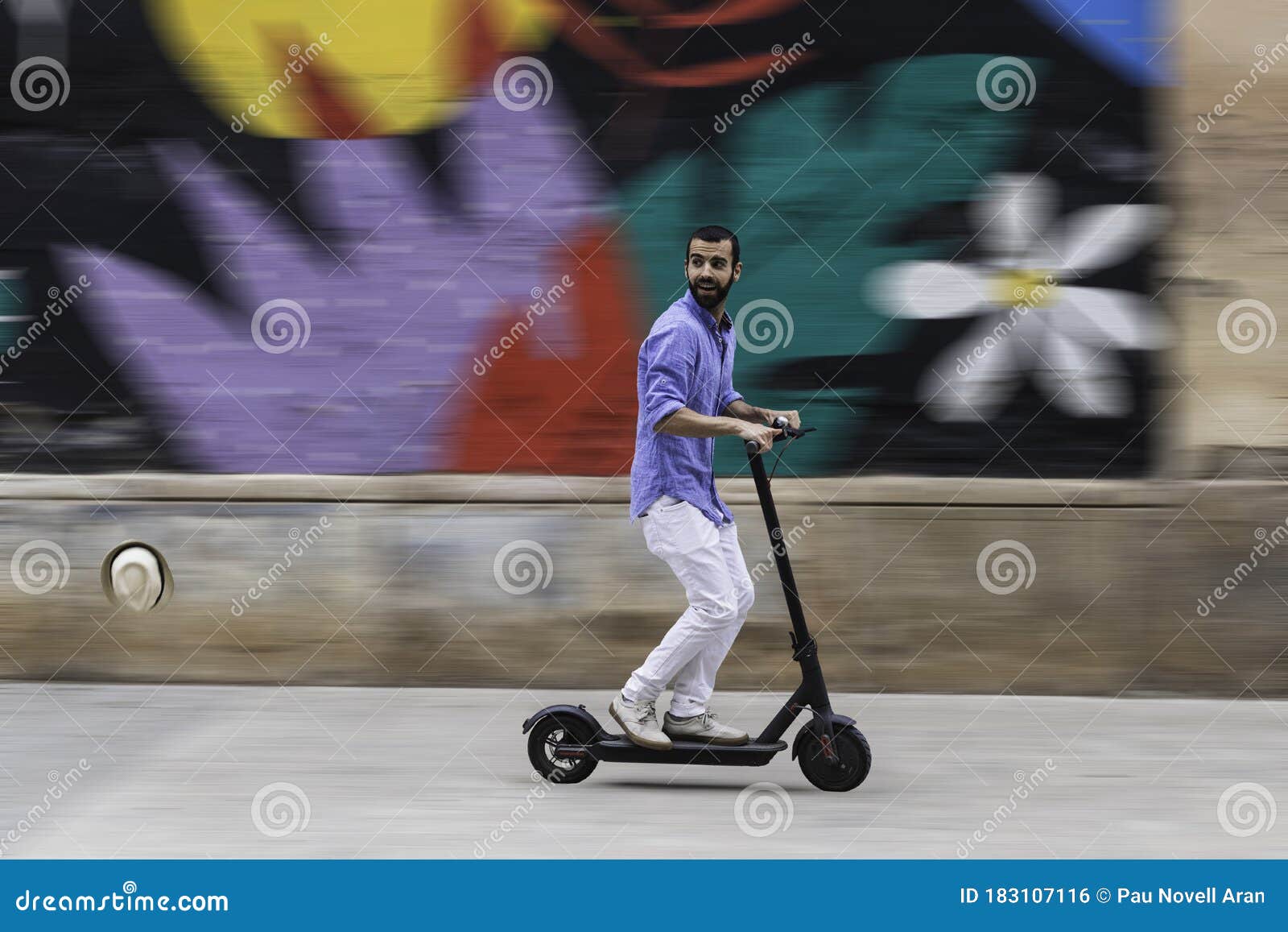 Man on Electric Scooter Losing His Hat. Background with Blurred Motion