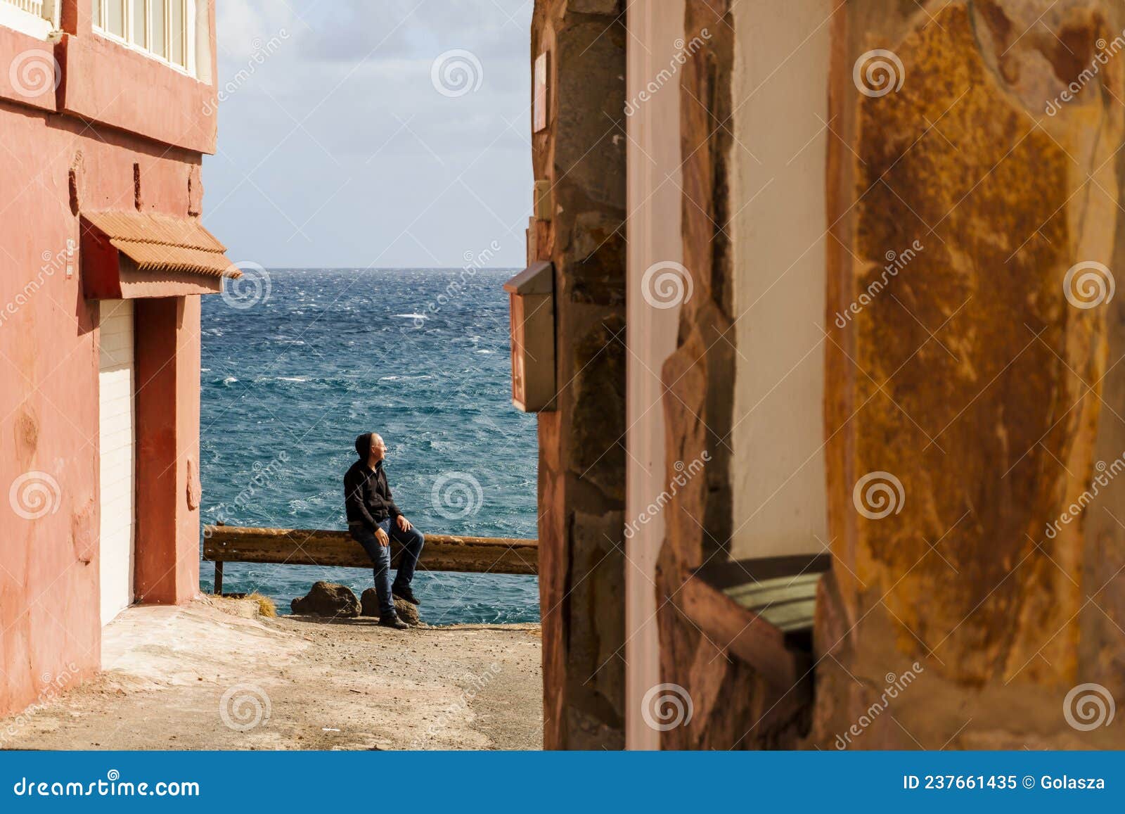 a man enjoying the sun and the ocean sitting on the seaside railing in pozo izquierdo, canary islands, spain
