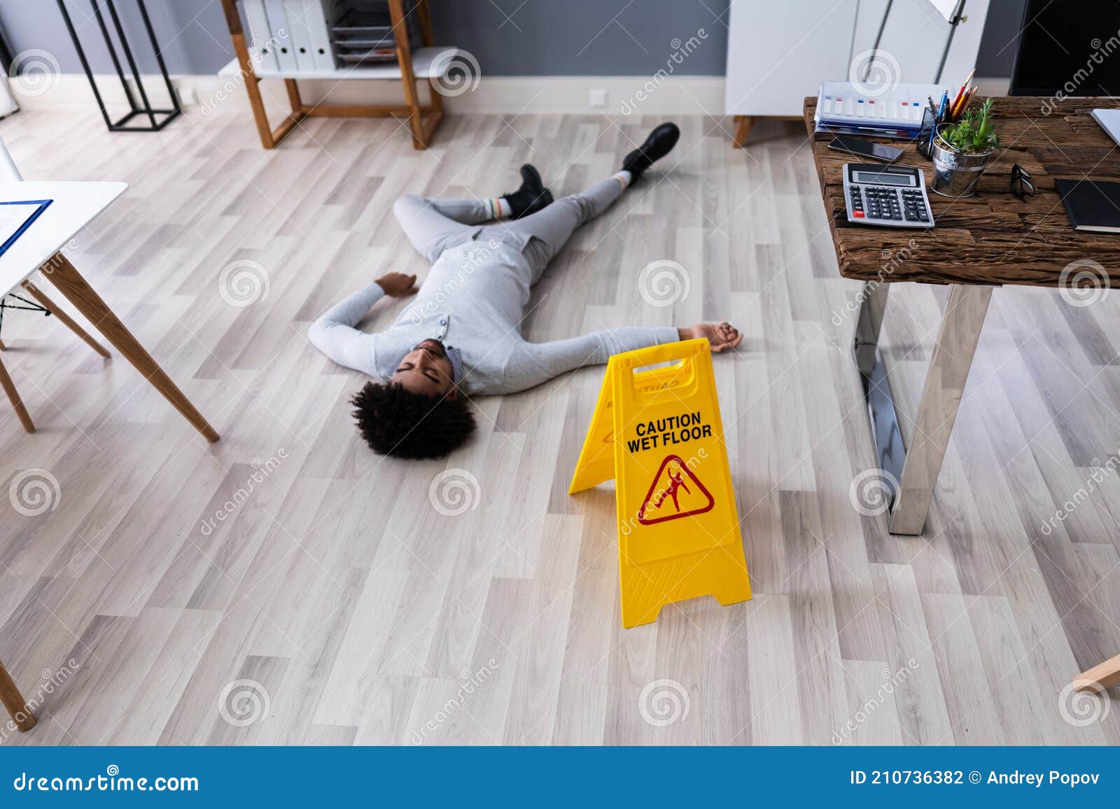 Man Falling on Wet Floor in Front of Caution Sign Stock Photo Image