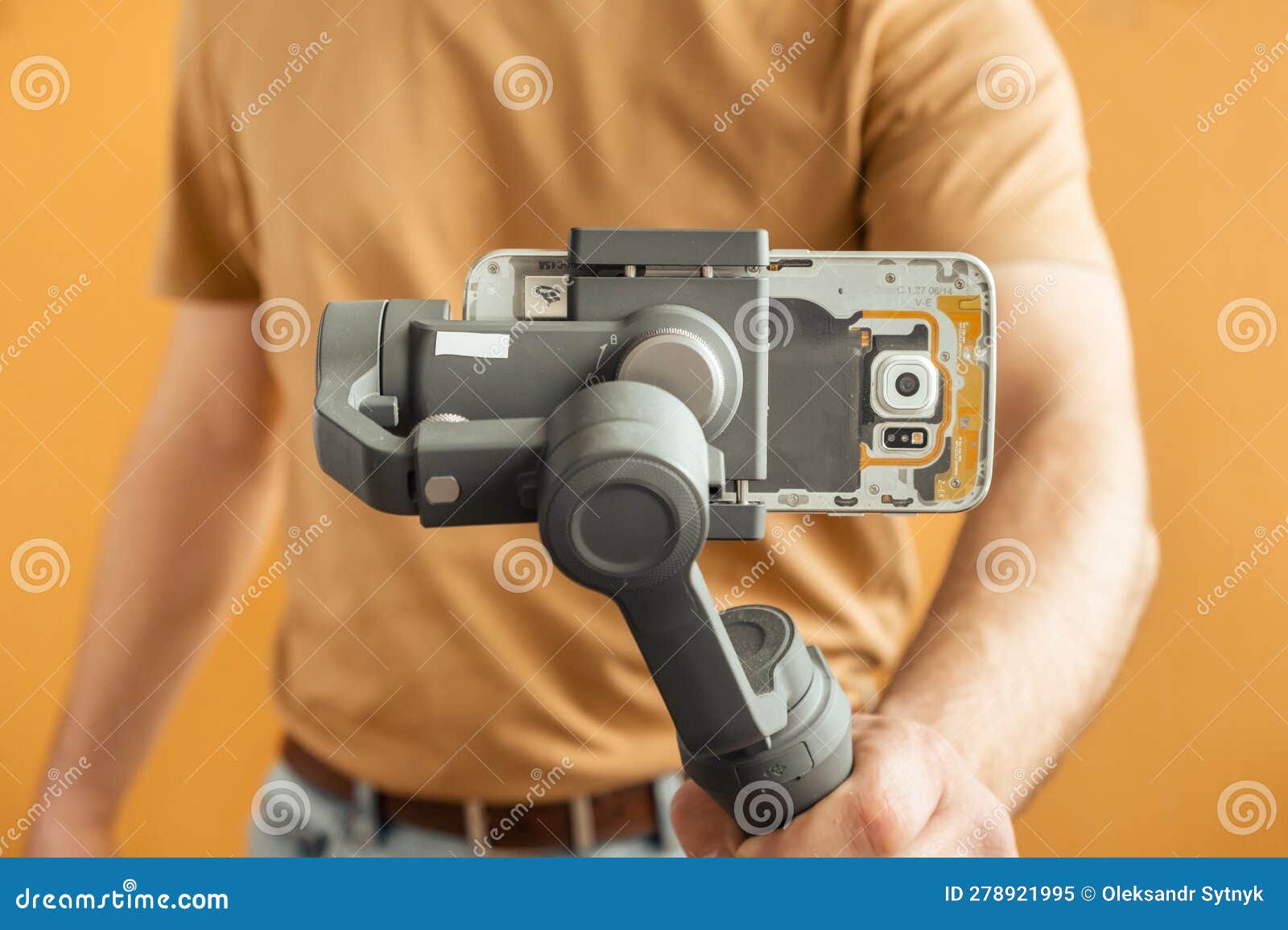 man filming with a smartphone using a gimbal stabilizer on yellow background. using three-axis electronic stabilizer to make vlogs