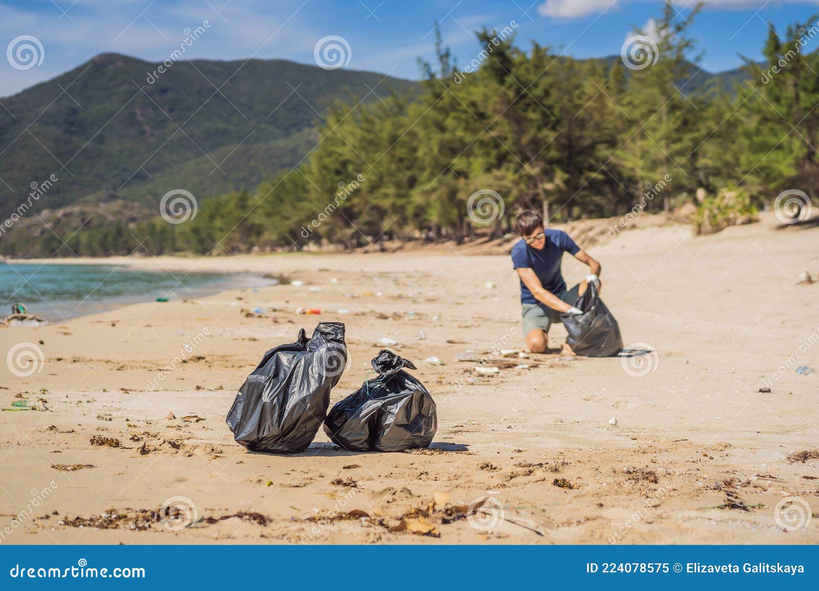 man in gloves pick up plastic bags that pollute sea. problem of spilled rubbish trash garbage on the beach sand caused