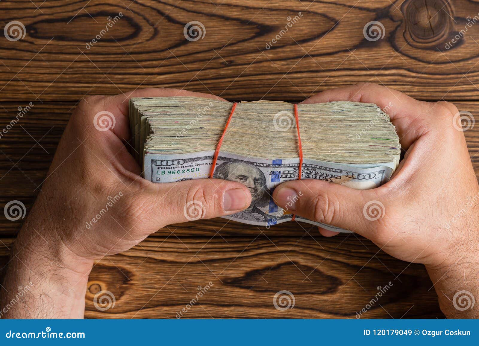 man gripping a thick stack of 100 dollar bills
