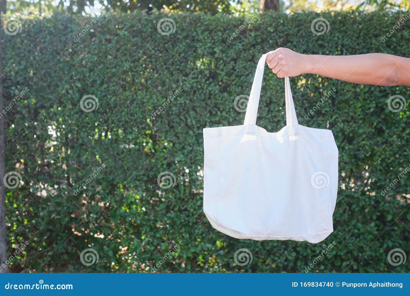 man hand holding a blank organic cotton tote bag on nature background. reusable shopping bags is good for the environment concept