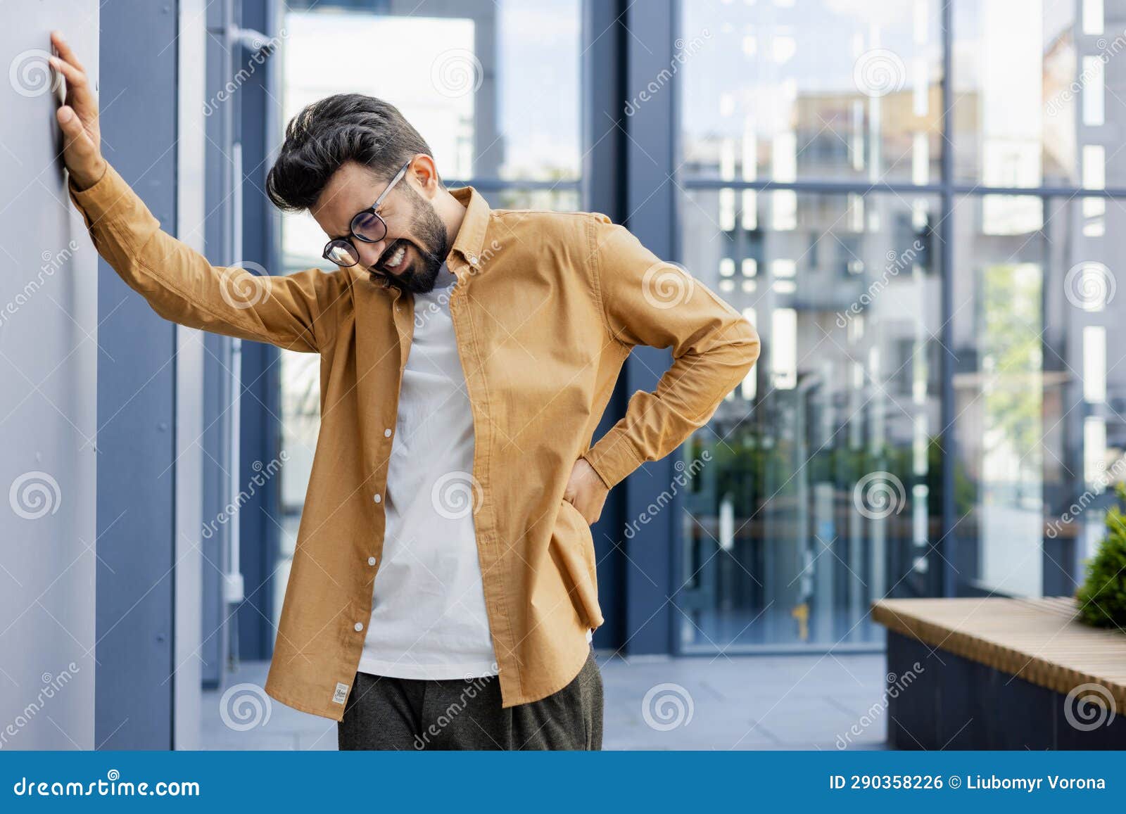 man has severe back pain, overtired and overworked worker from sedentary work, massaging his back with his hand