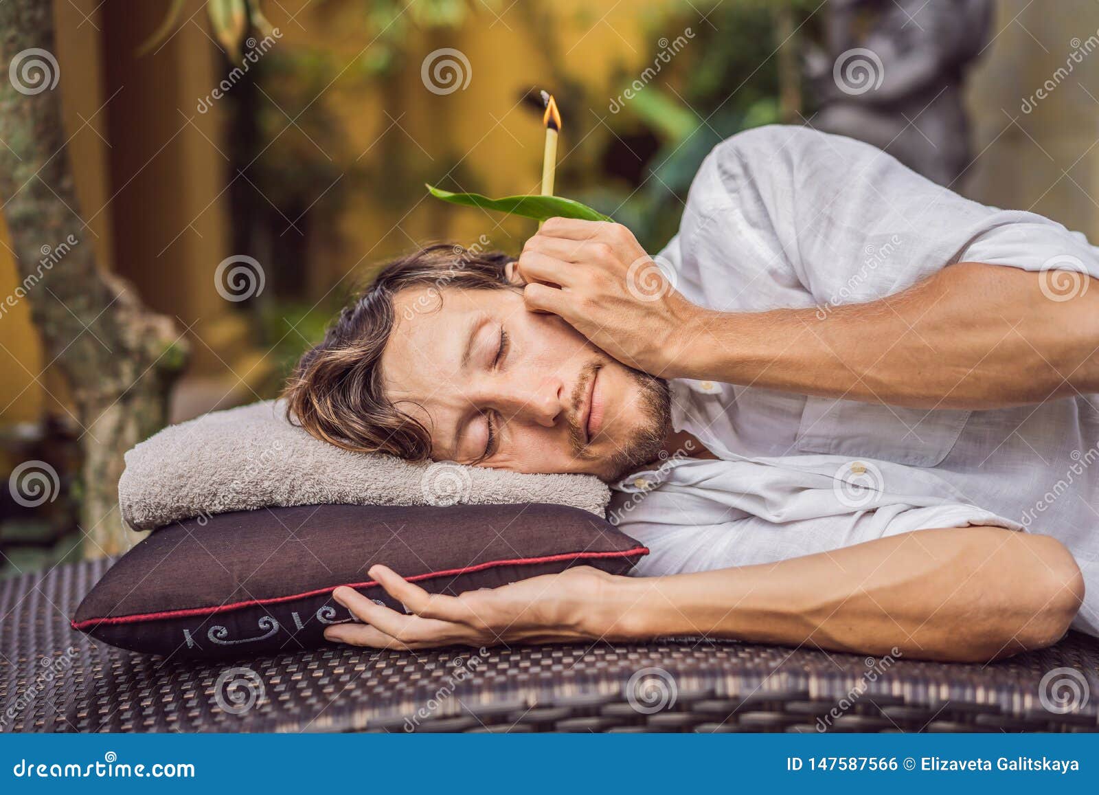 Man Having an Ear Candle Therapy Against the Backdrop of a Tropical