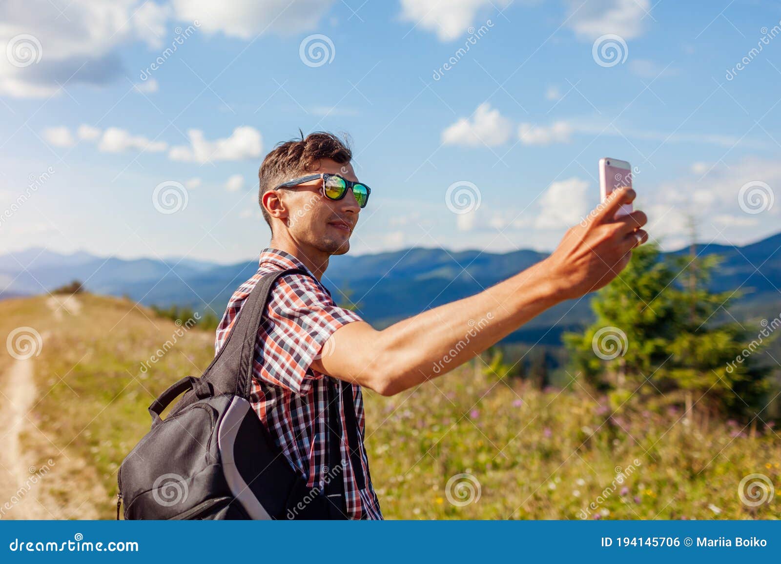 man hiker taking selfie with smartphone in carpathian mountains on hill peak. traveler backpaker enjoys view