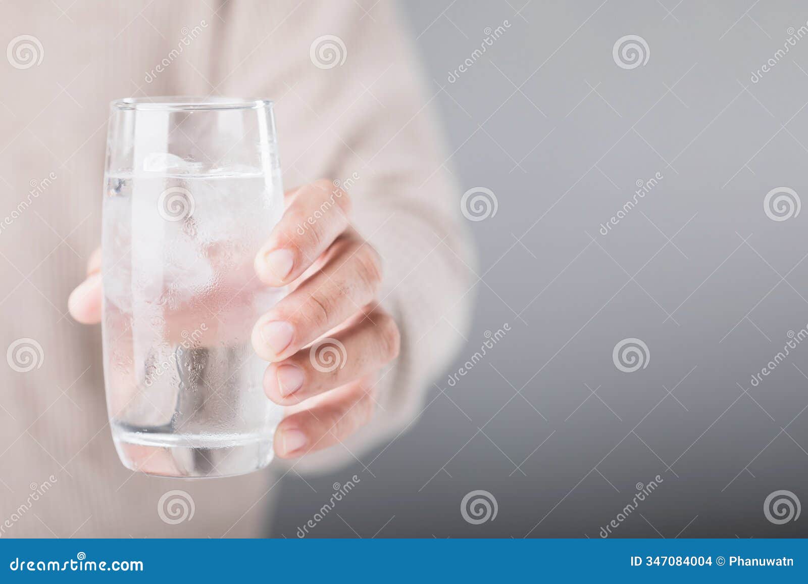 man holding a glass of cold water with ice, showing a slight grimace due to tooth sensitivity. image reflects the discomfort of