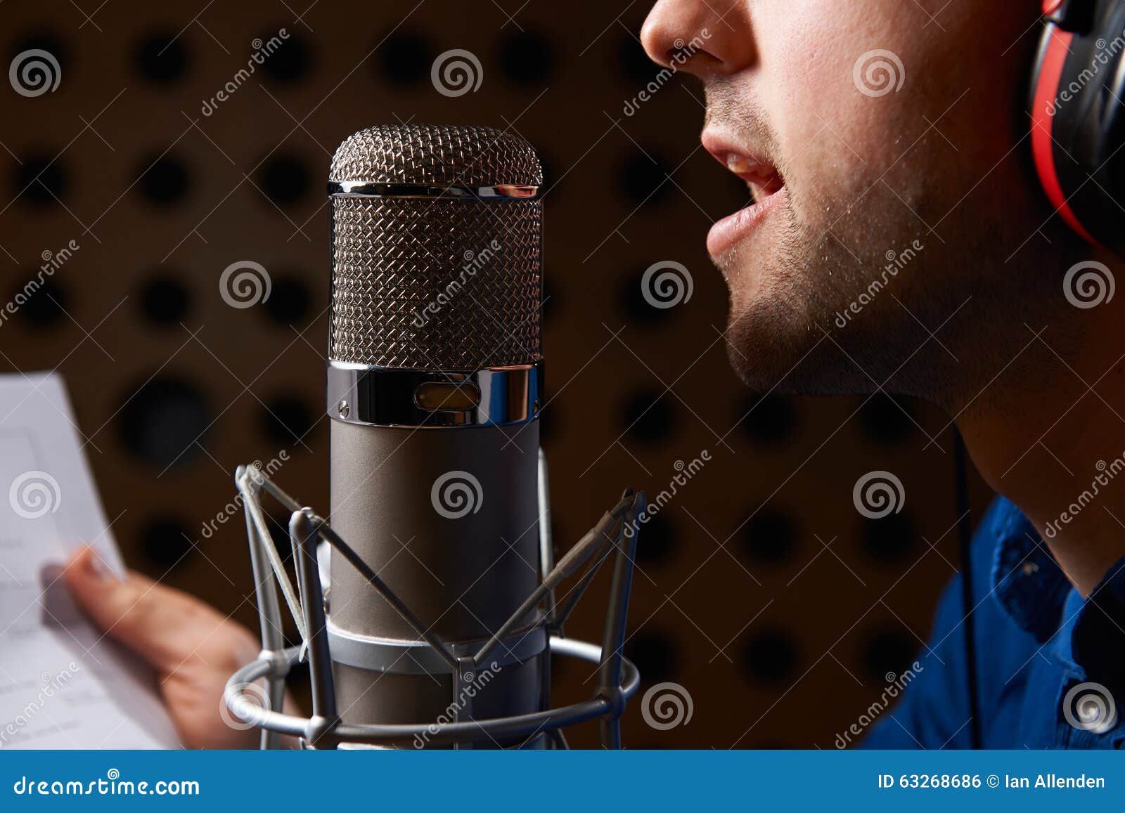 Man Holding Notes and Talking into Studio Microphone Stock Photo