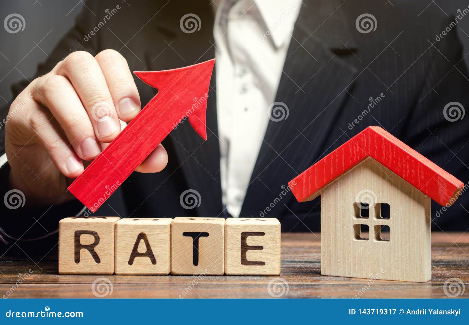 a man holds a red arrow up above the word rate and a wooden house. the concept of raising interest rates on mortgages. the