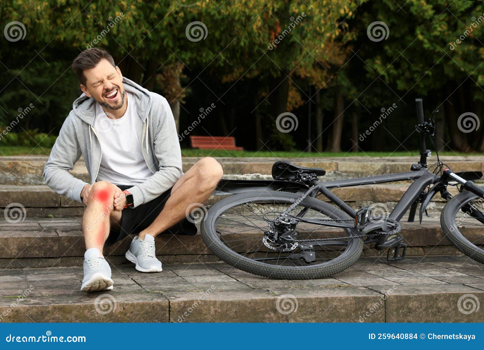 Man with Injured Knee on Steps Near Bicycle Outdoors Stock Photo