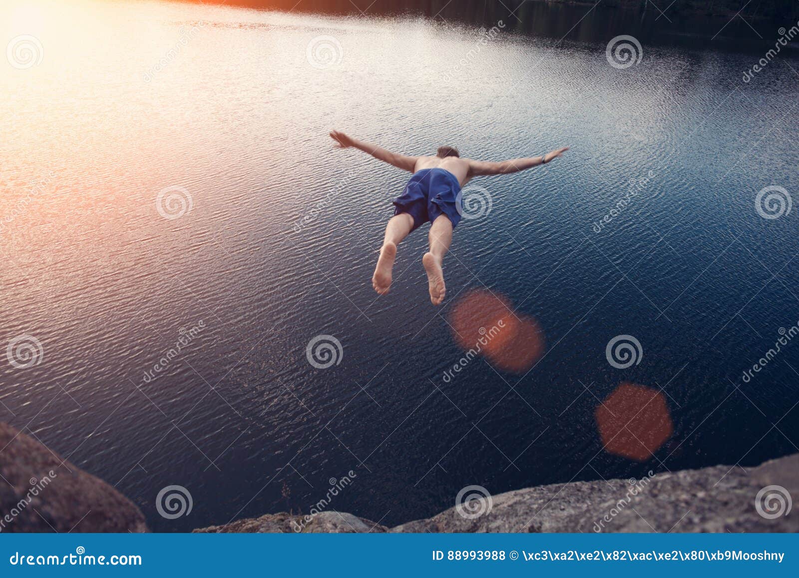 man jumping into the water from cliff at sunset with outspread hands