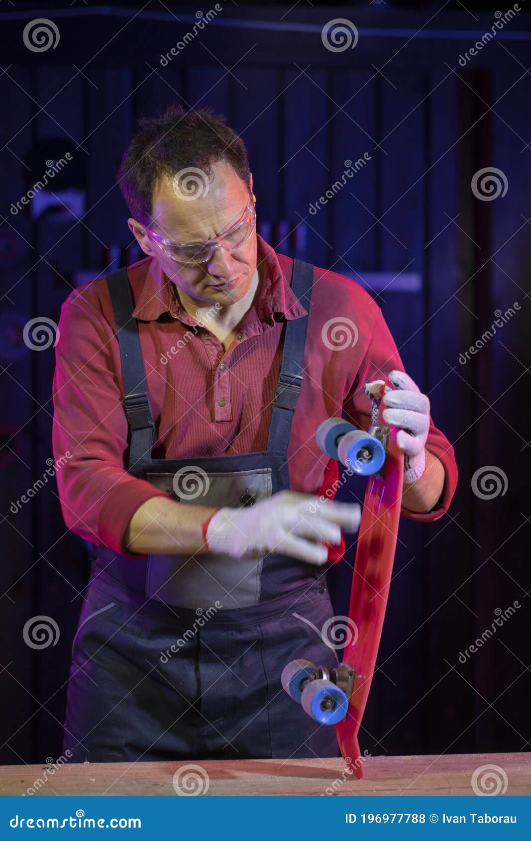 man in jumpsuit testing weels of plastic kids skateboard in home workshop