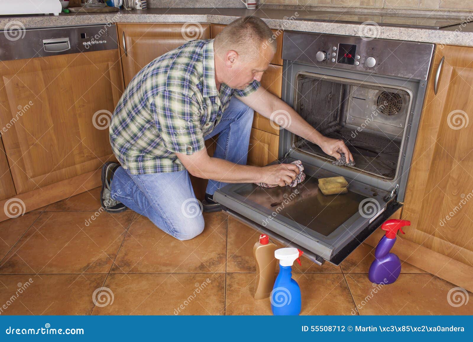 Man Kneels On The Floor In The Kitchen And Cleans The Oven 