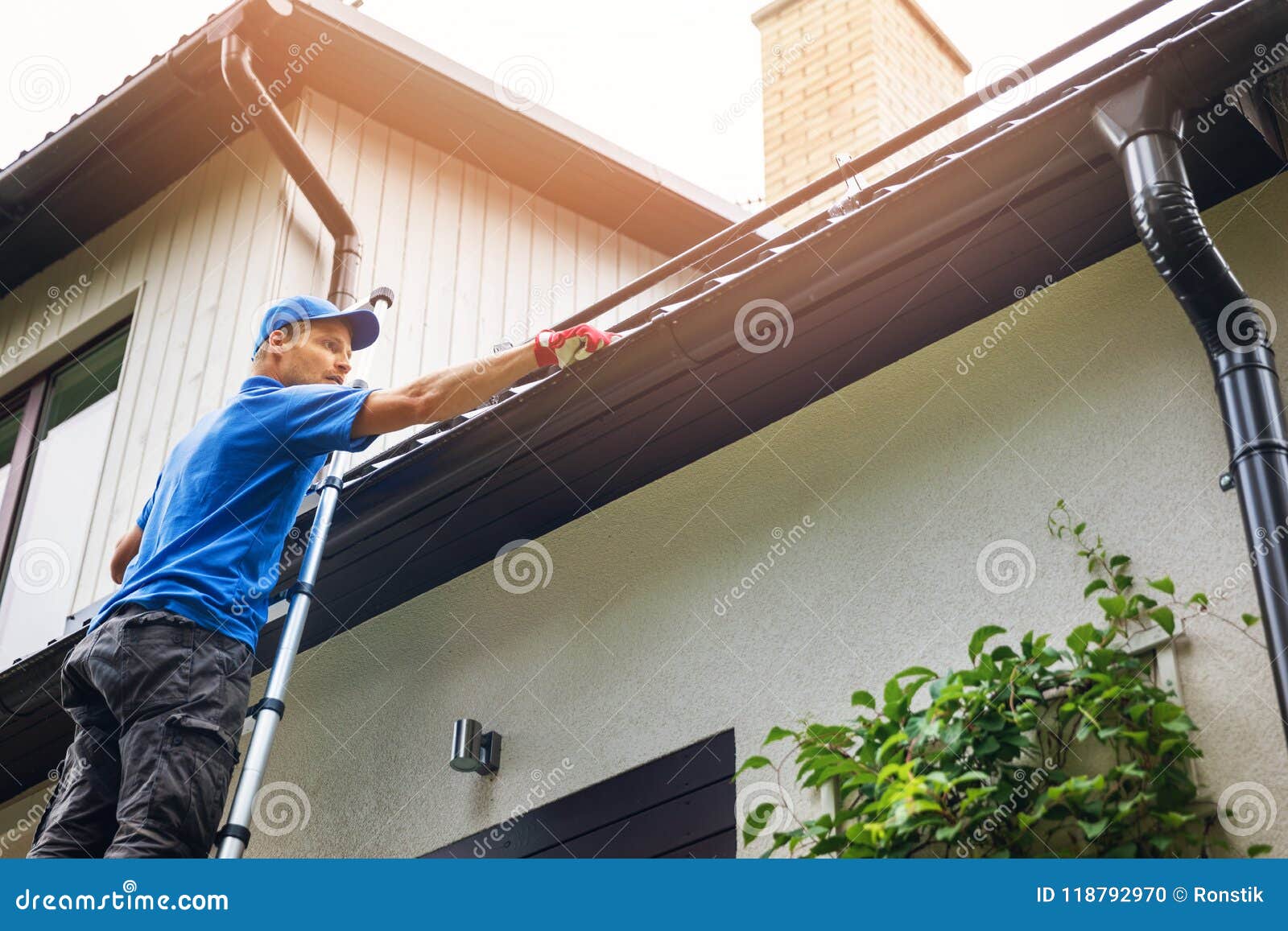 man on ladder cleaning house gutter
