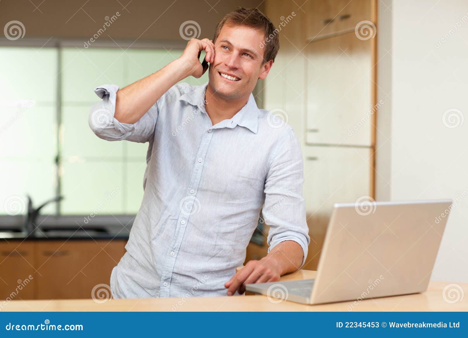 Smiling man with laptop and cellphone in the kitchen