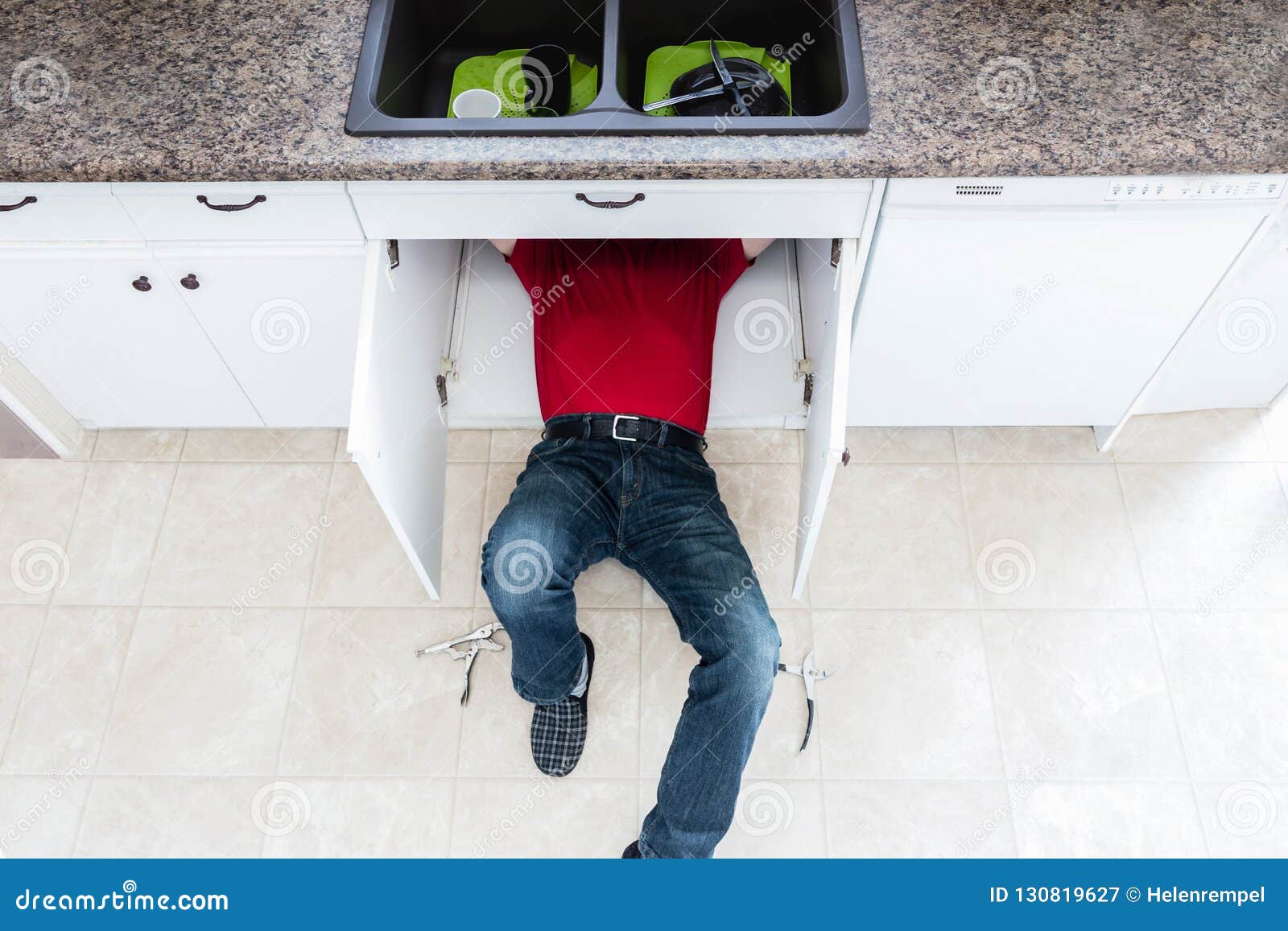 Man Lying On The Floor Under The Kitchen Sink Fixing A Leak Stock