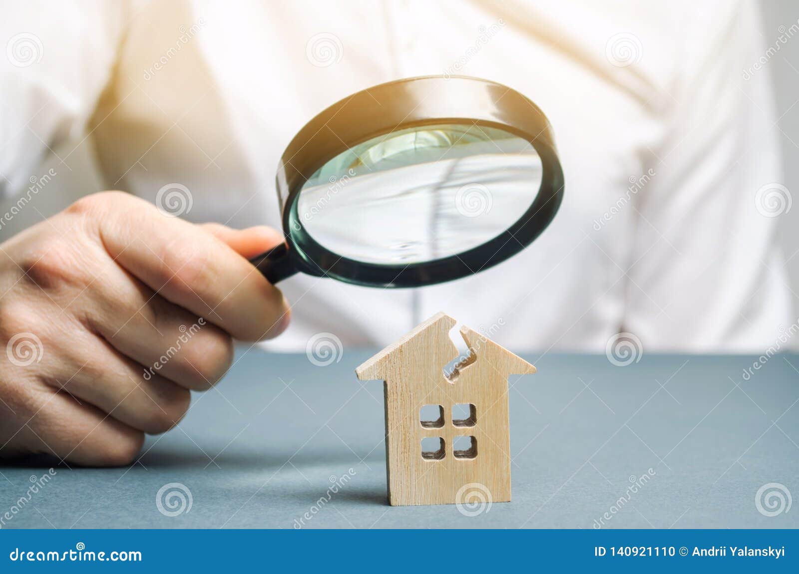 a man with a magnifying glass looks at a house with a crack. damage assessment home and insurance risks