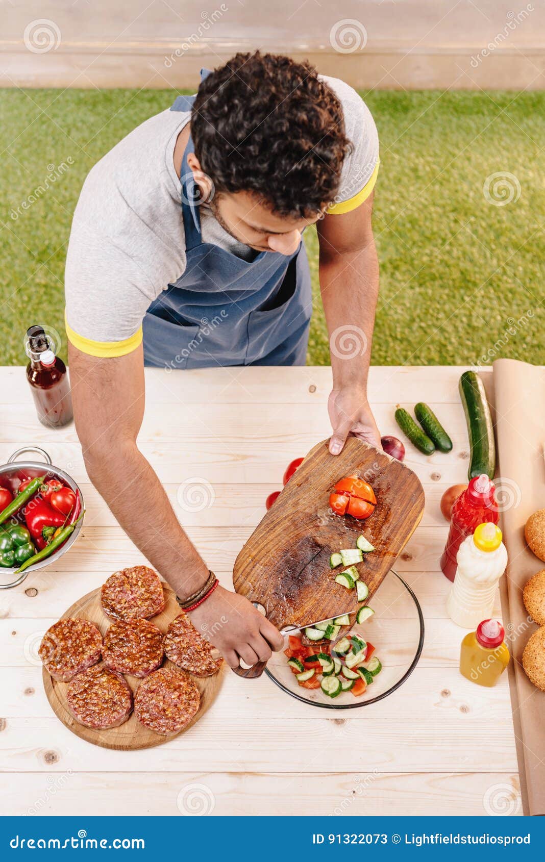 Man Making Burgers and Cutting Red Tomatoes Outdoors Stock Image