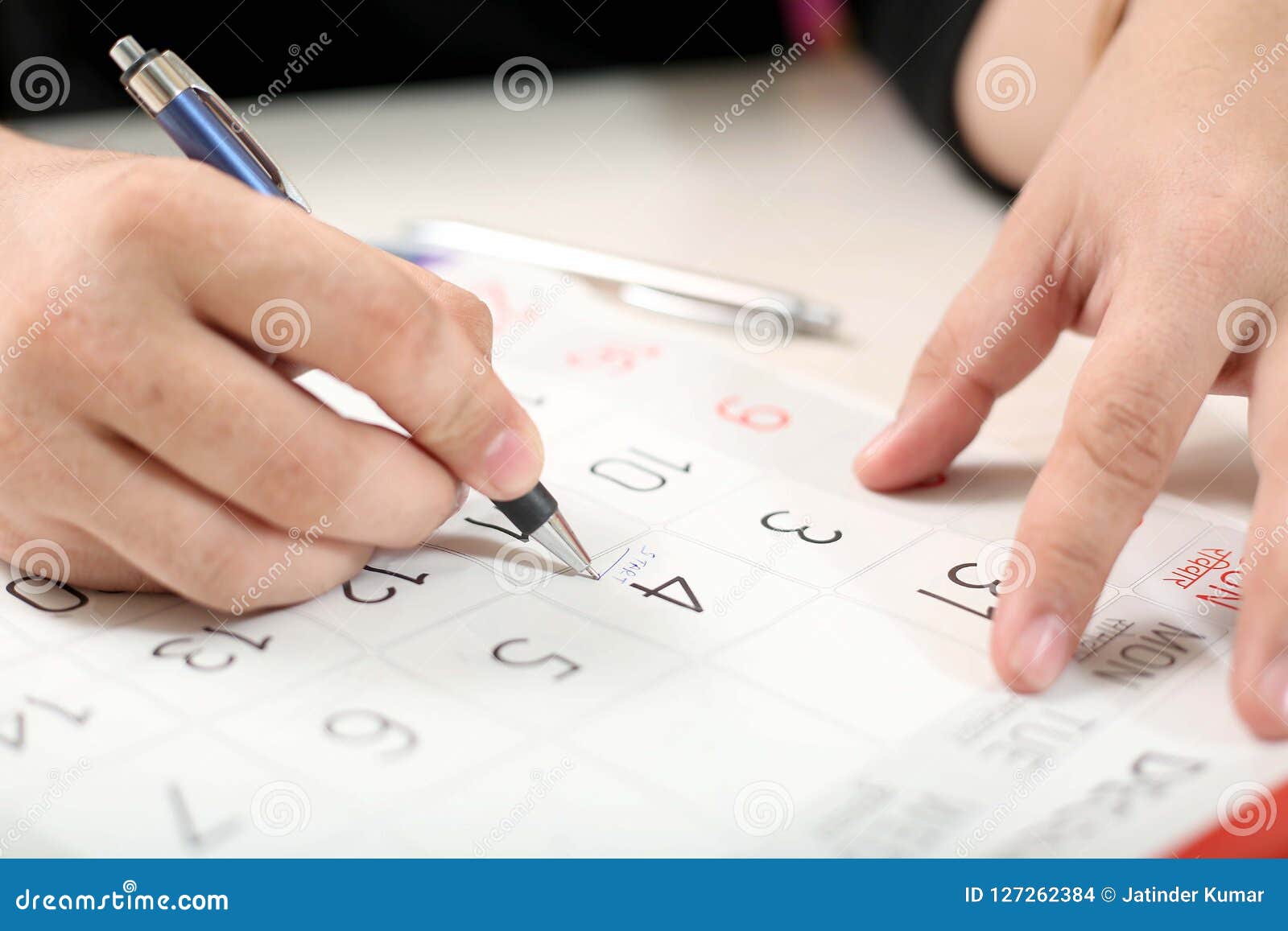 Man is Marking Date on Calendar for Schedule with Pen Stock Photo