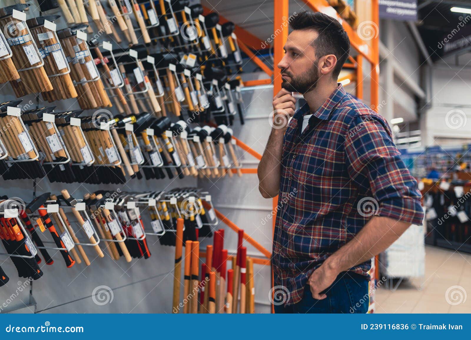 A Man Next To a Rack with Hammers in a Hardware Store Chooses a Tool