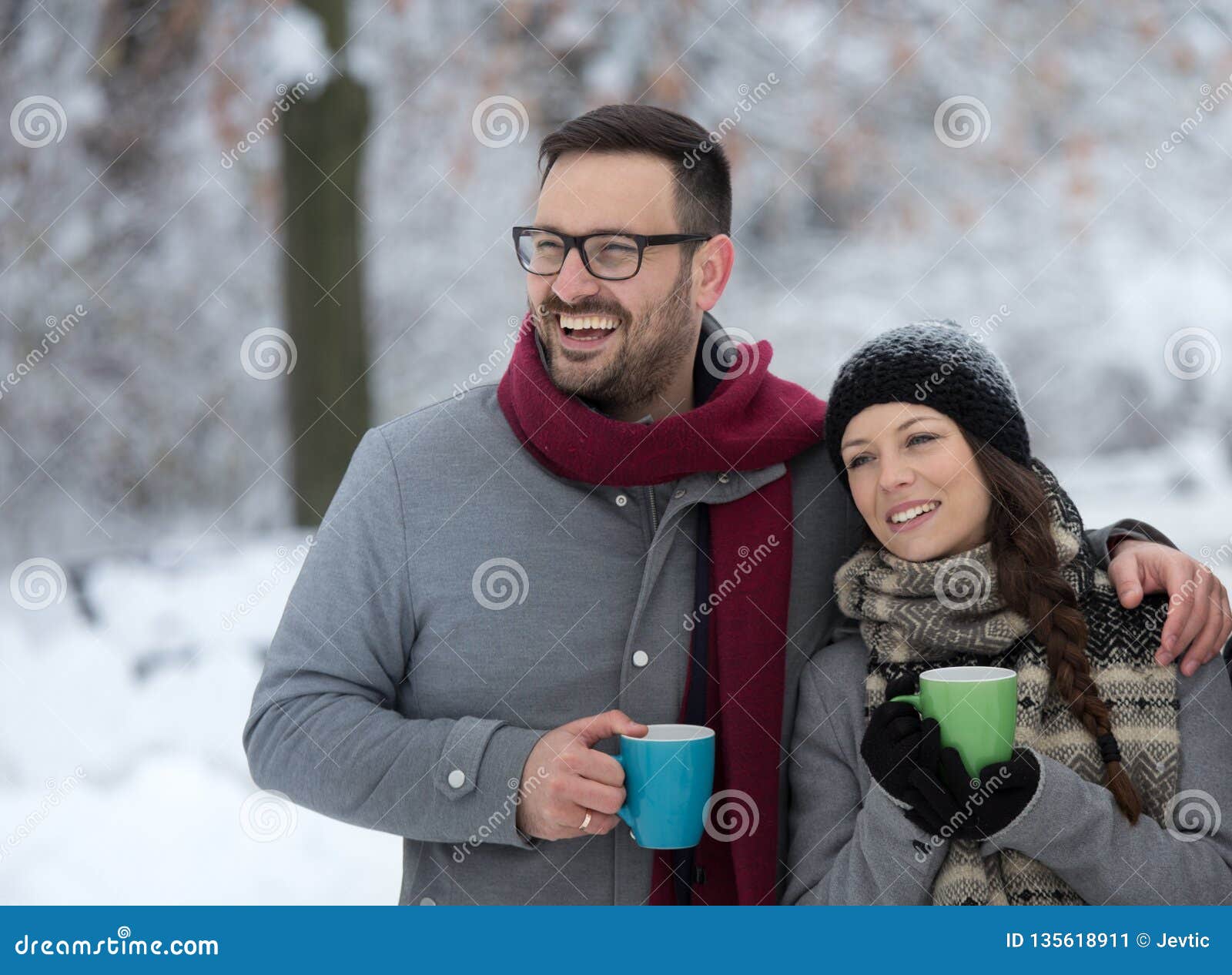 Man och kvinna med den varma drinken på snö. Hållande kopp för unga par av den varma drinken på insnöad skog