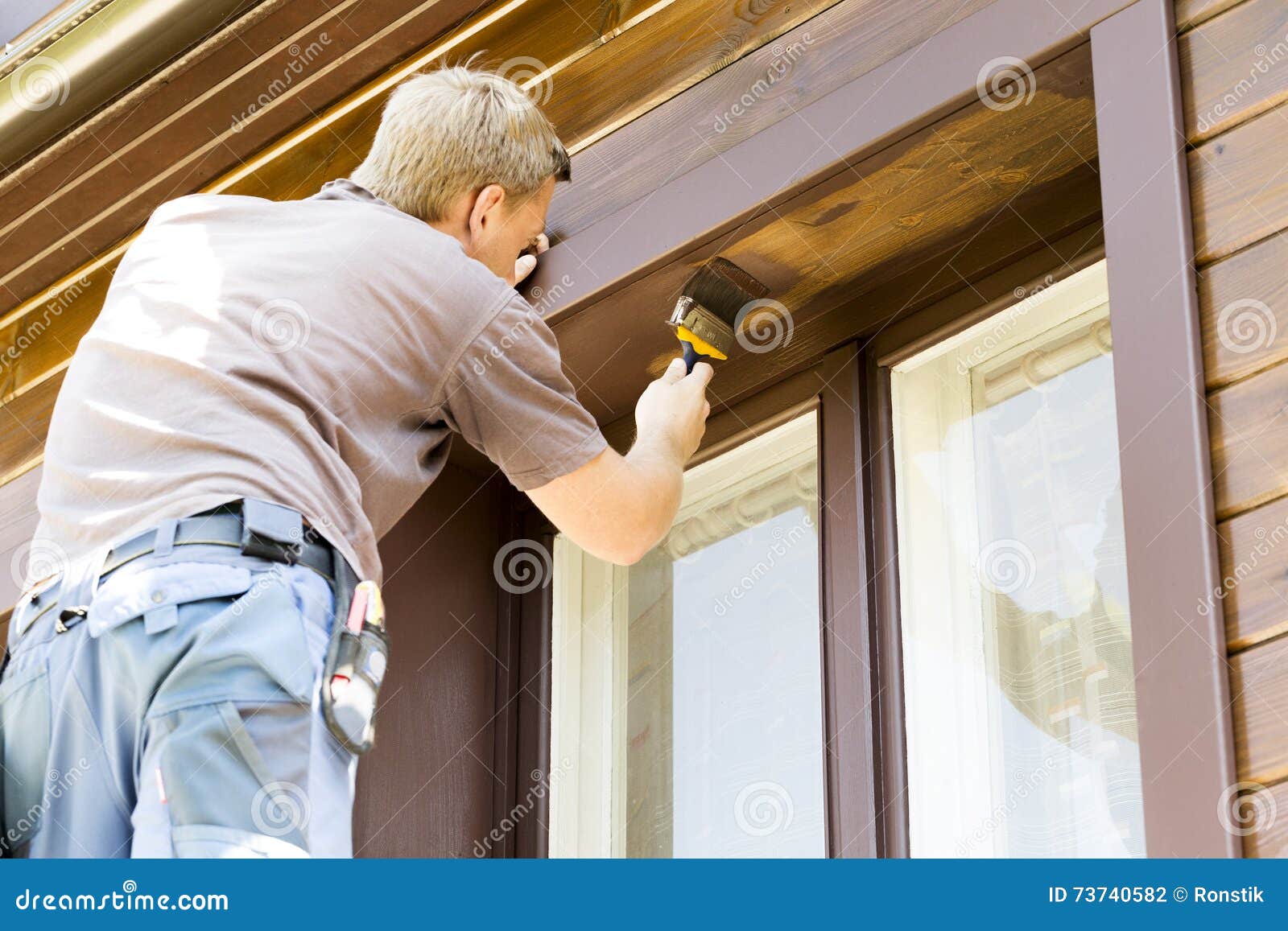 man with paintbrush painting wooden house exterior